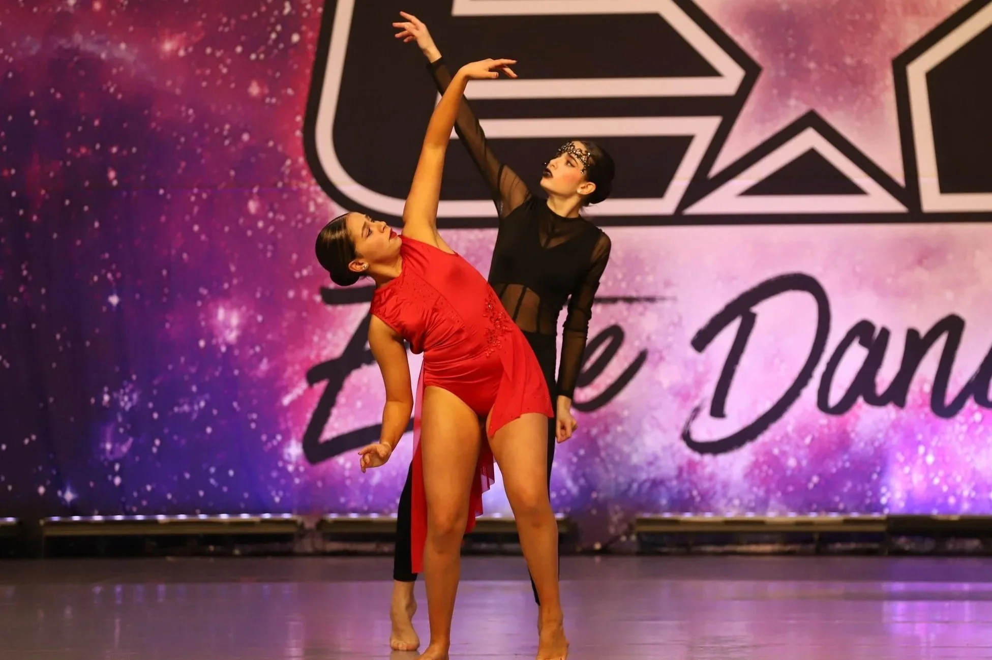 Two dancers perform a contemporary dance routine on stage with a colorful starry background and the words 'Dance Dance' displayed prominently.