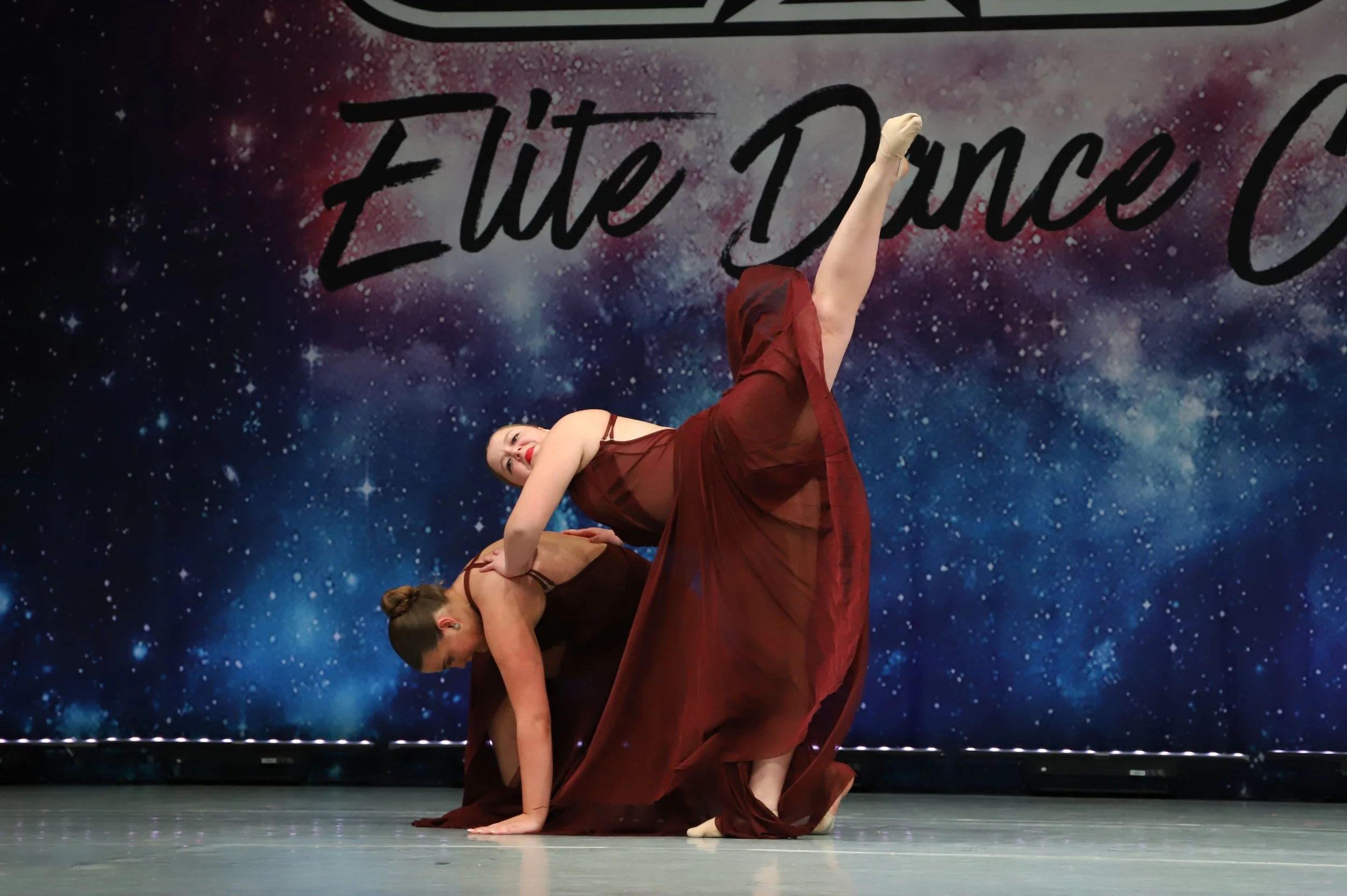 Three women performing a dance routine on stage, with a galaxy-themed backdrop that has the words "The Dance" written on it.