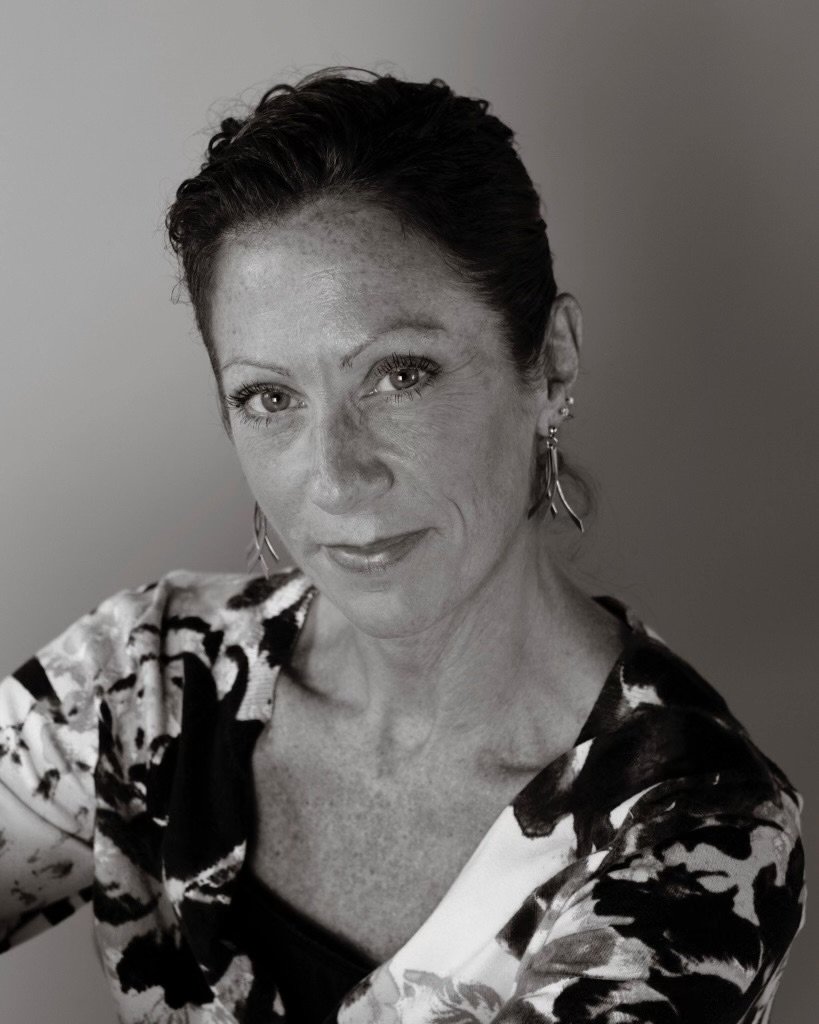 A black-and-white portrait of a woman with short dark hair, wearing earrings, a patterned top, and smiling slightly.
