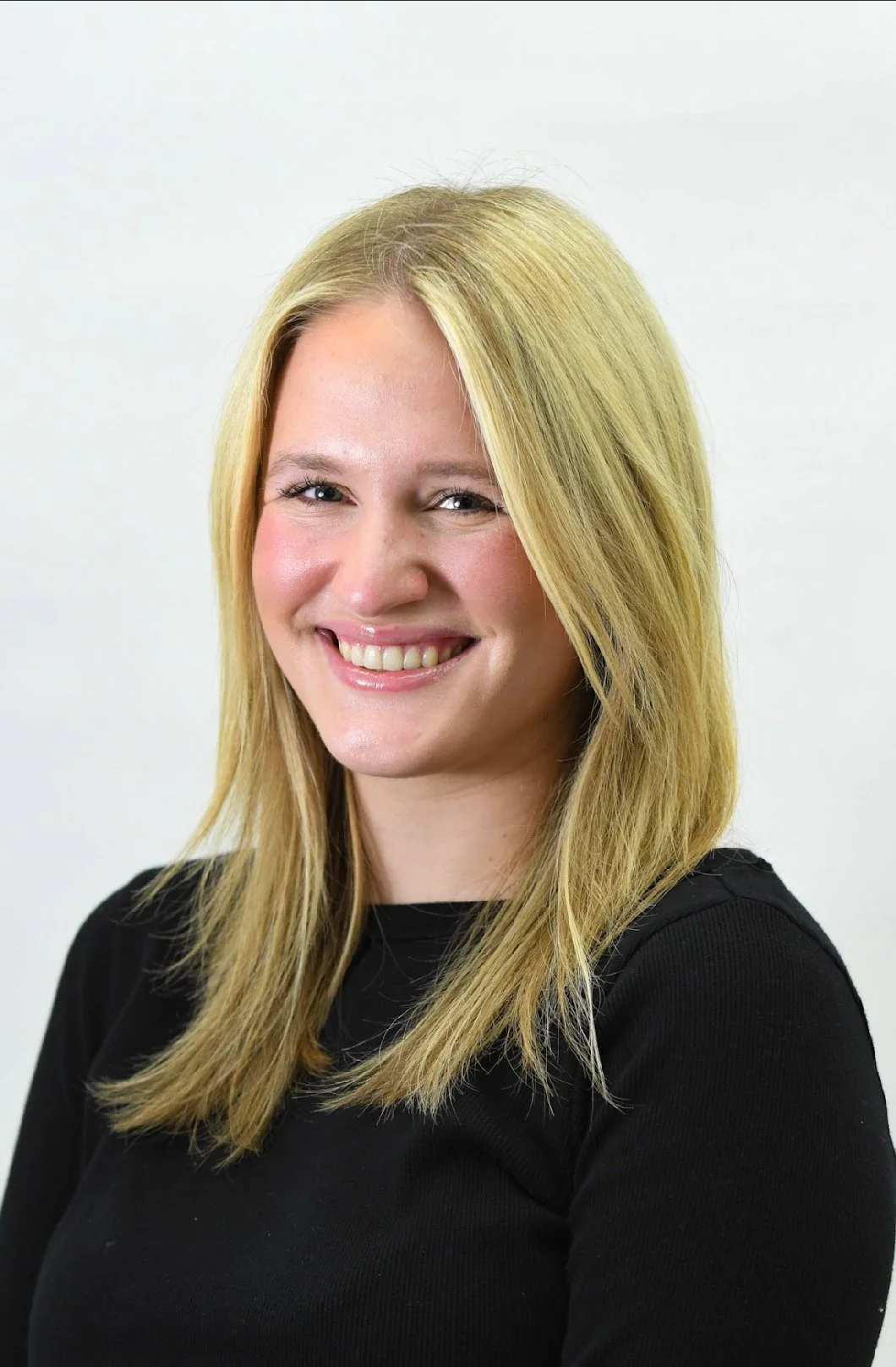 A smiling woman with blonde hair wearing a black top against a white background.