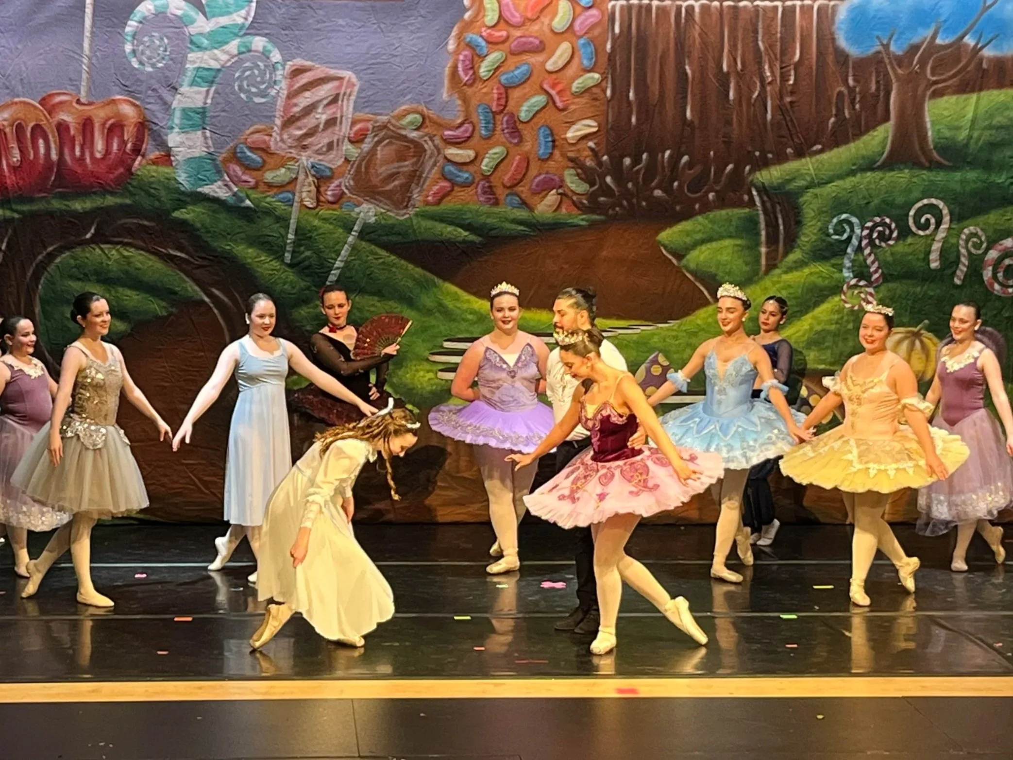 Ballet dancers performing on stage with a colorful, whimsical backdrop featuring candy and candy cane motifs and trees.