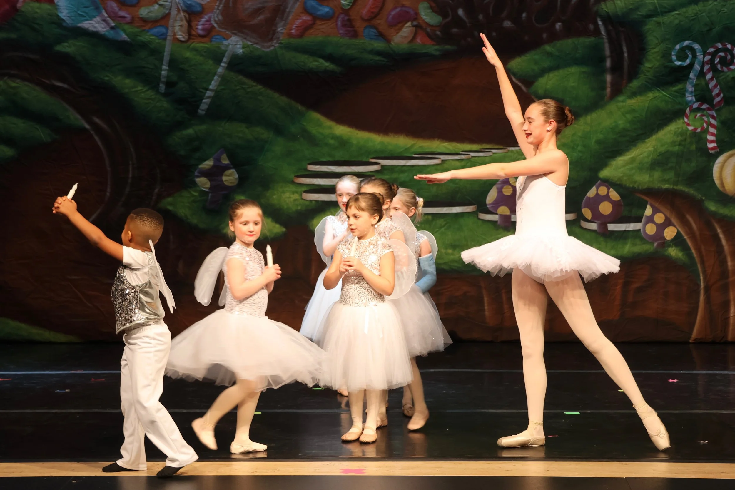 Ballet dancers performing on stage, with a backdrop of a colorful enchanted forest scene.