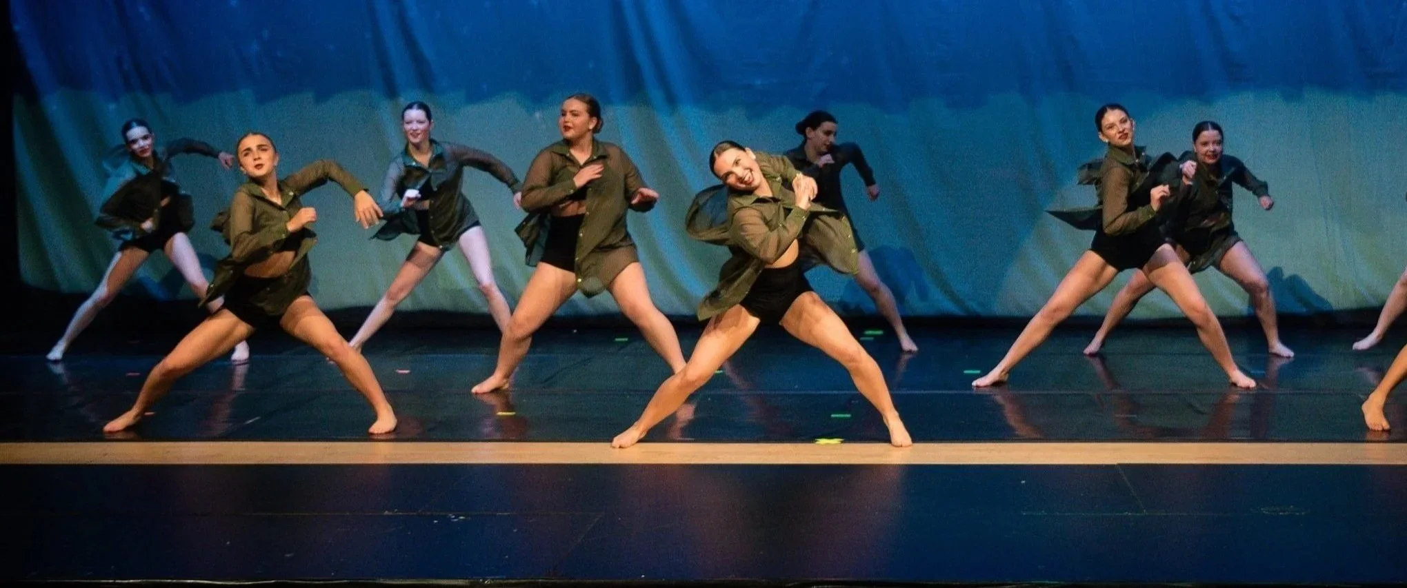 Dance group performing on stage, wearing military-inspired costumes, with a blue backdrop.
