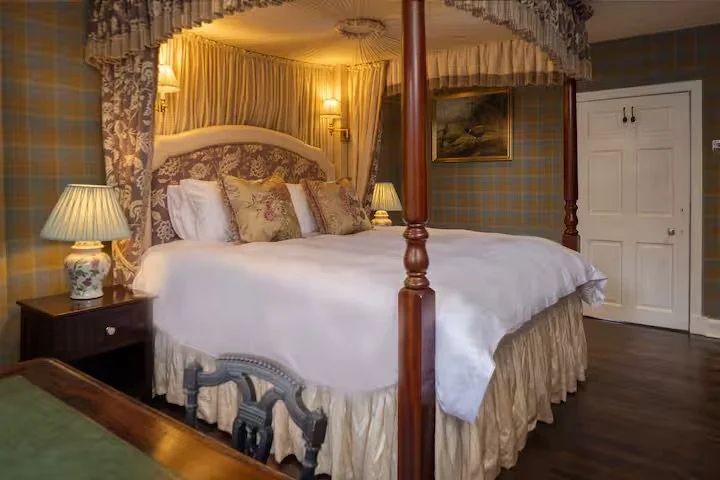 Elegant bedroom featuring a four-poster bed with white linens and decorative pillows, bedside lamps, and floral curtains.