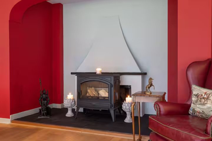 Living room with red and white walls, a black fireplace with candles on top, and decorative items including a horse figurine and a pillow on a red leather armchair.