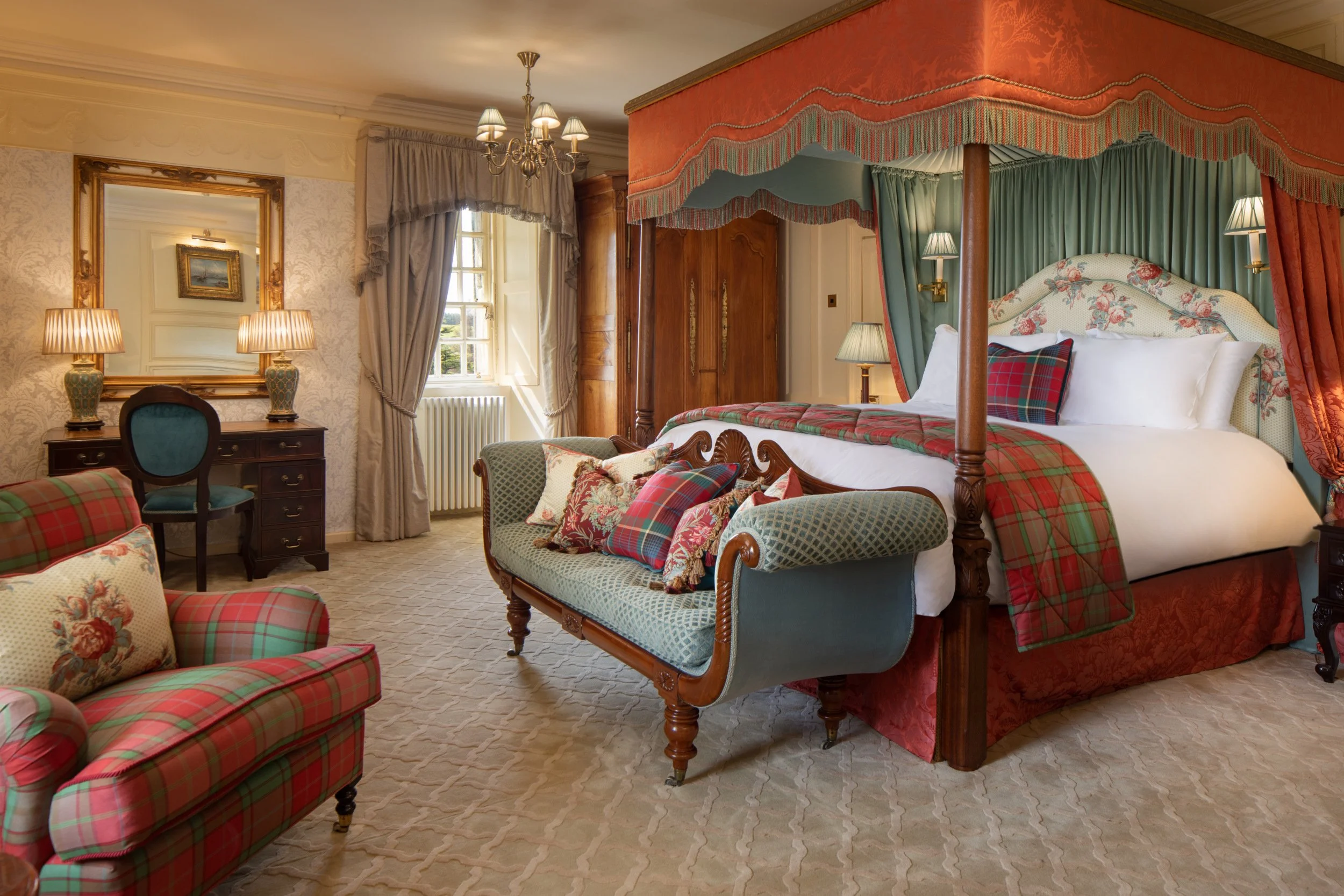 Elegant bedroom with a canopy bed, patterned drapes, upholstered chairs, a mirror, lamps, and a chandelier in a classic decor style.