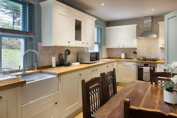 Bright kitchen with white cabinets, wooden countertops, stainless steel appliances, and a wooden dining table with chairs.