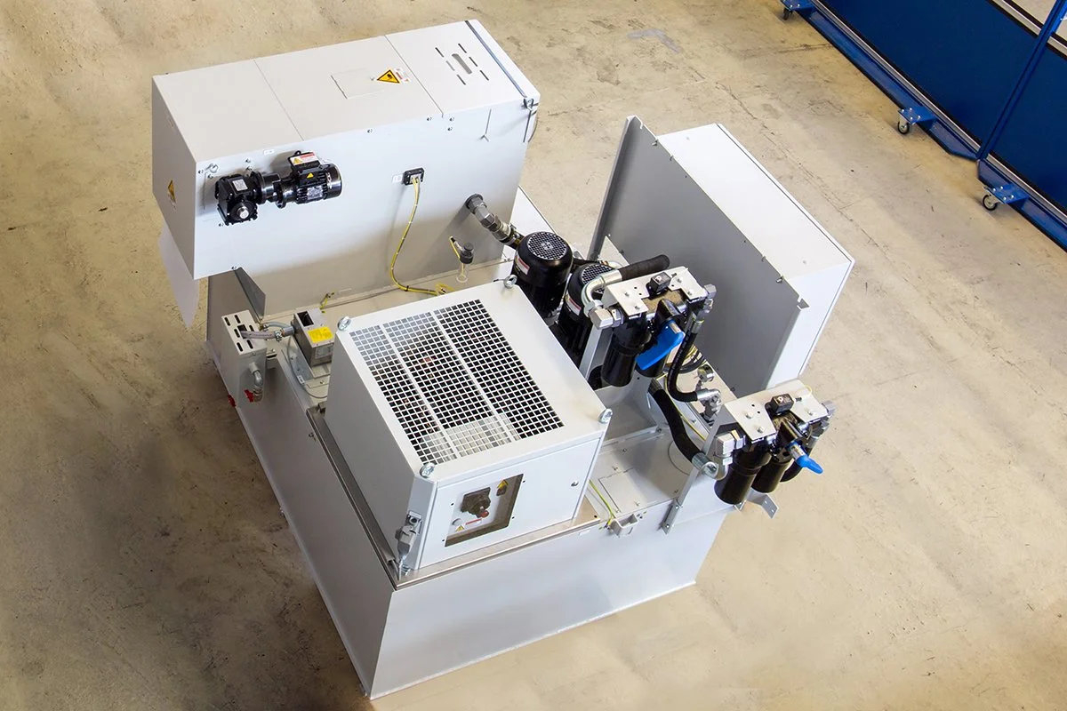 Technische Maschine mit Steuerung und Hydraulikkomponenten in einer Industrielagerhalle.