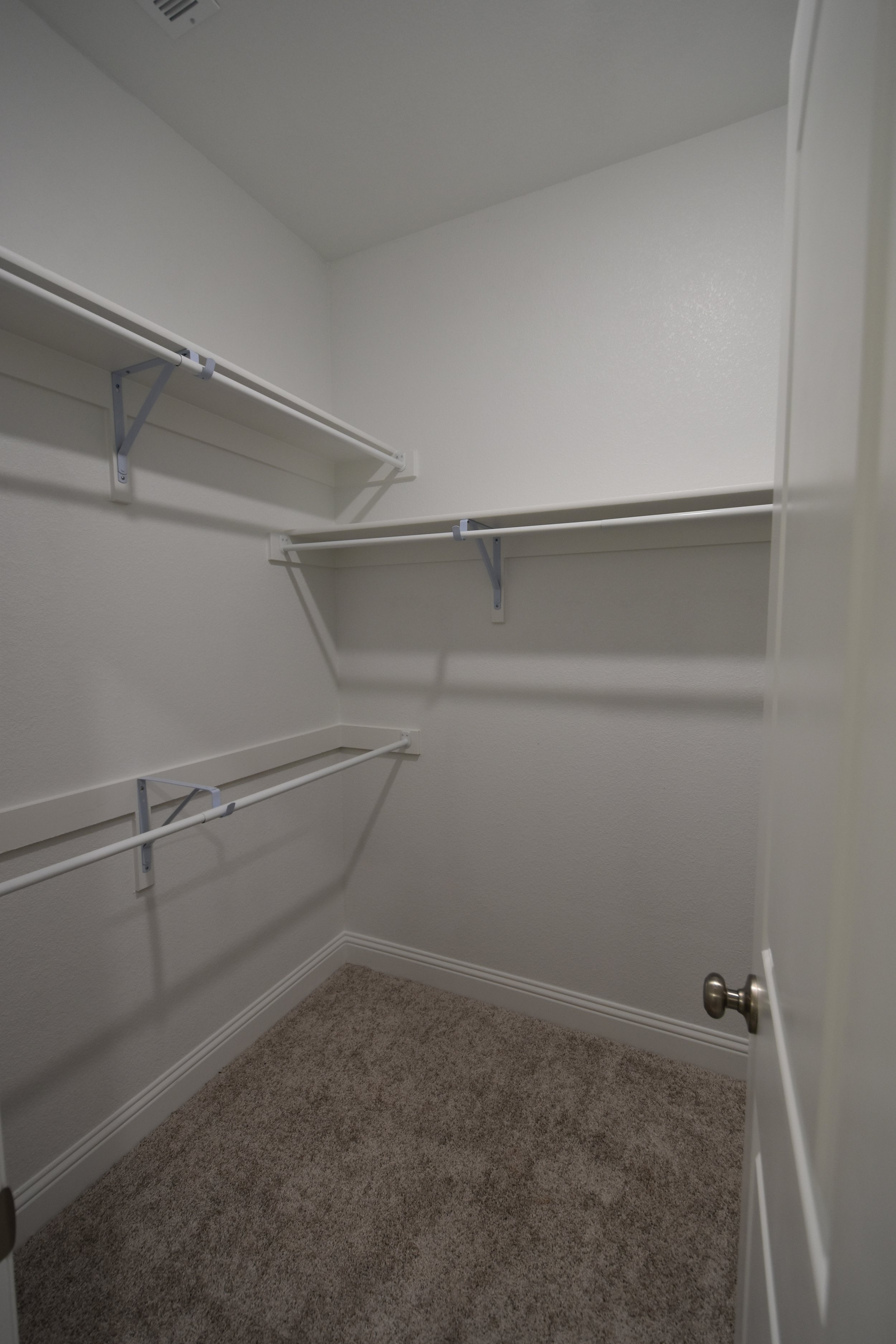 Empty walk-in closet with white wire shelves and beige carpet flooring.