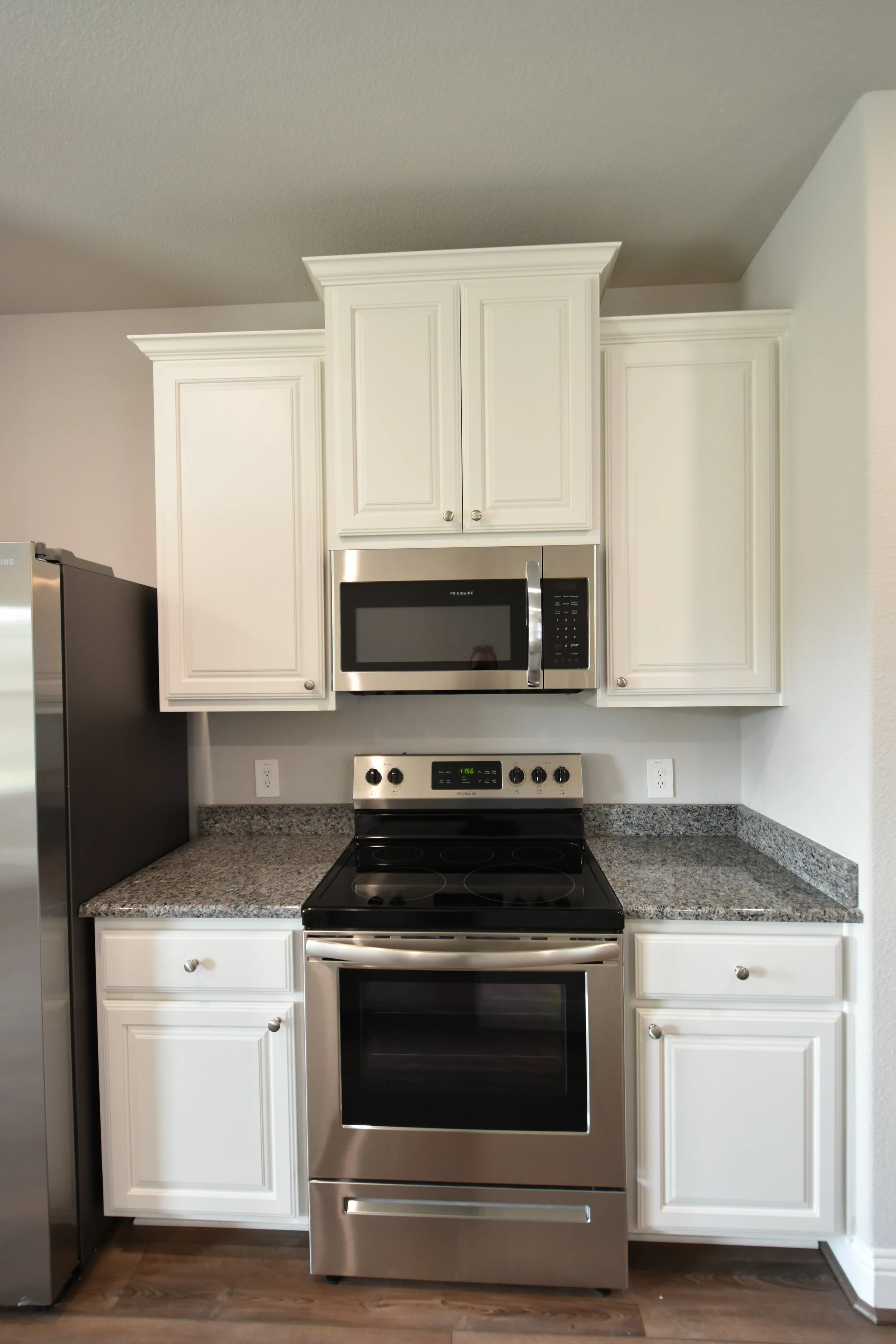 Stainless steel stove with black cooktop in front of white kitchen cabinets, microwave above, granite countertops, and hardwood floor.