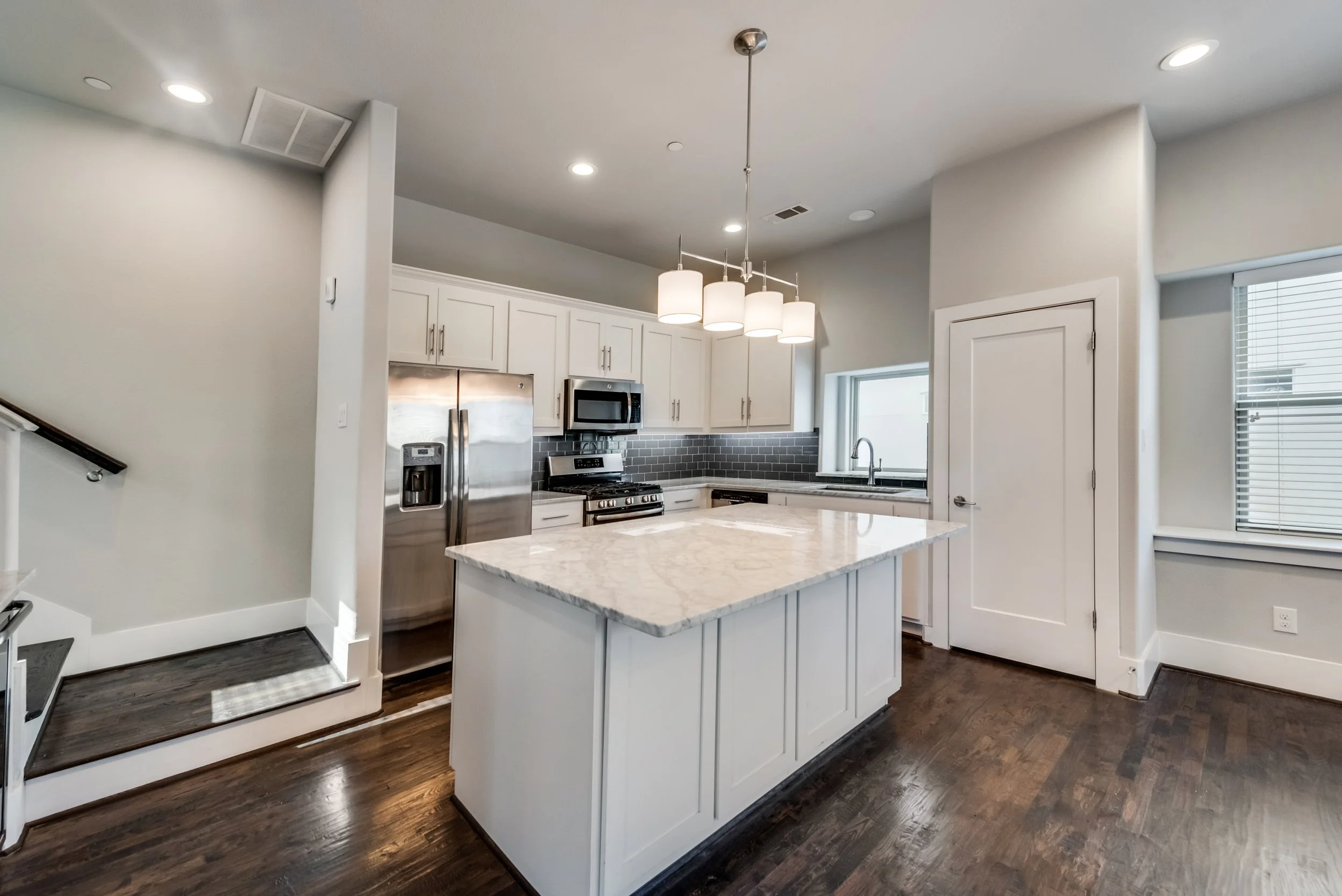 Modern kitchen with white cabinets, stainless steel appliances, a marble island, and dark hardwood floors.