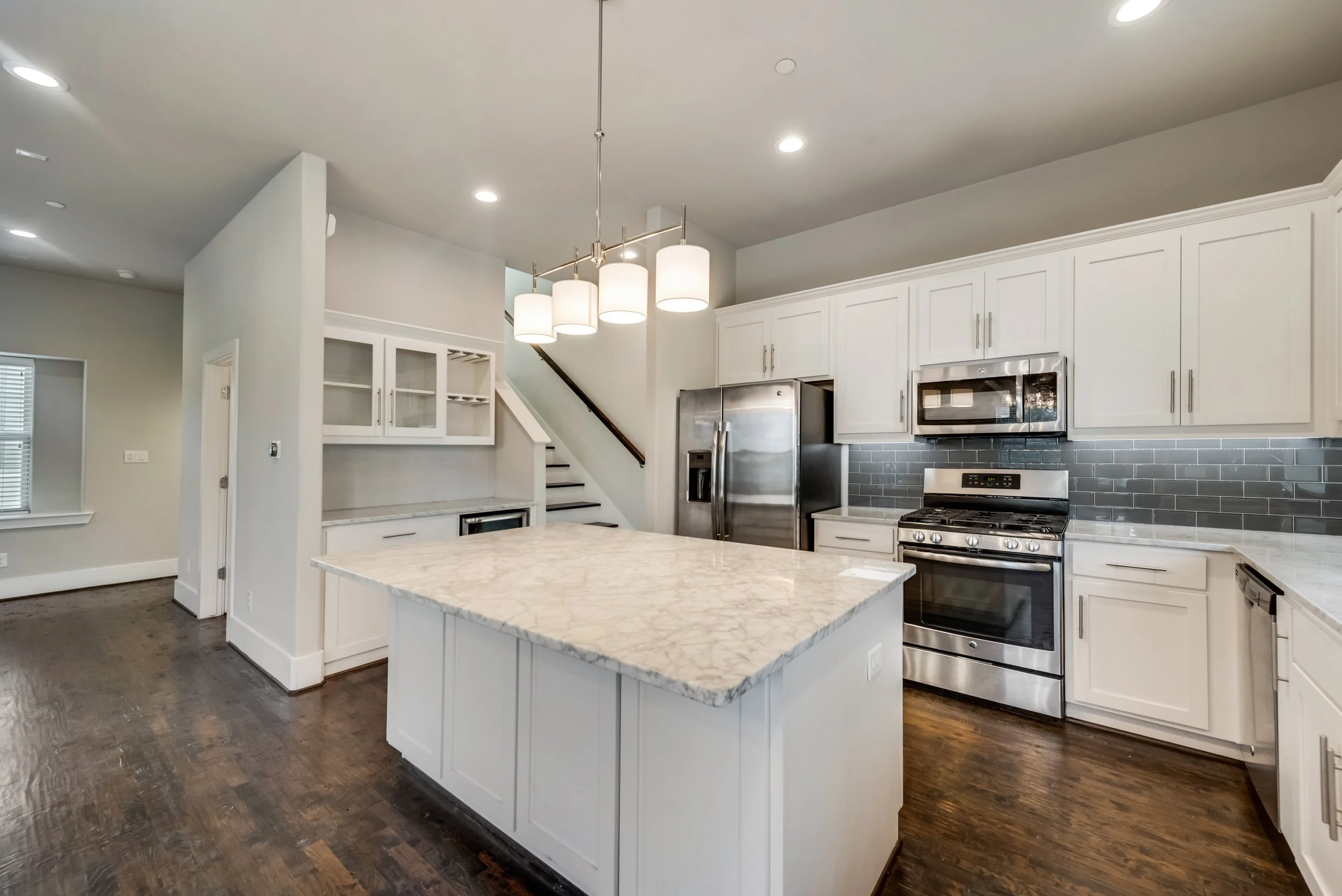 Modern kitchen with white cabinets, stainless steel appliances, a marble island, and a hanging light fixture.
