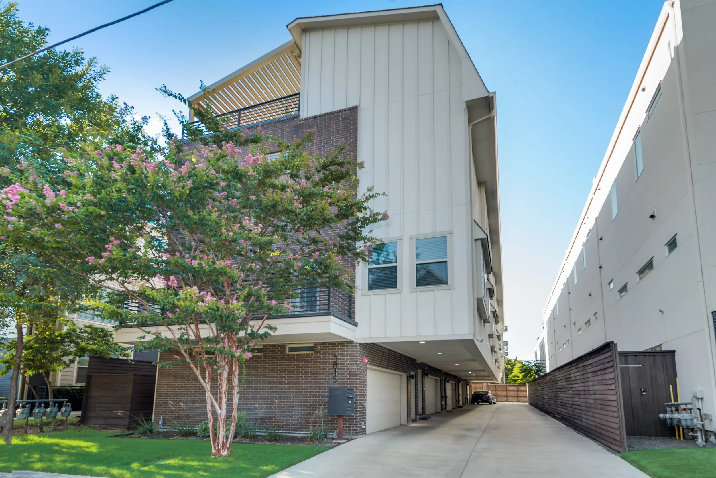 Modern apartment building with a tree with pink flowers in the foreground and a clear blue sky.