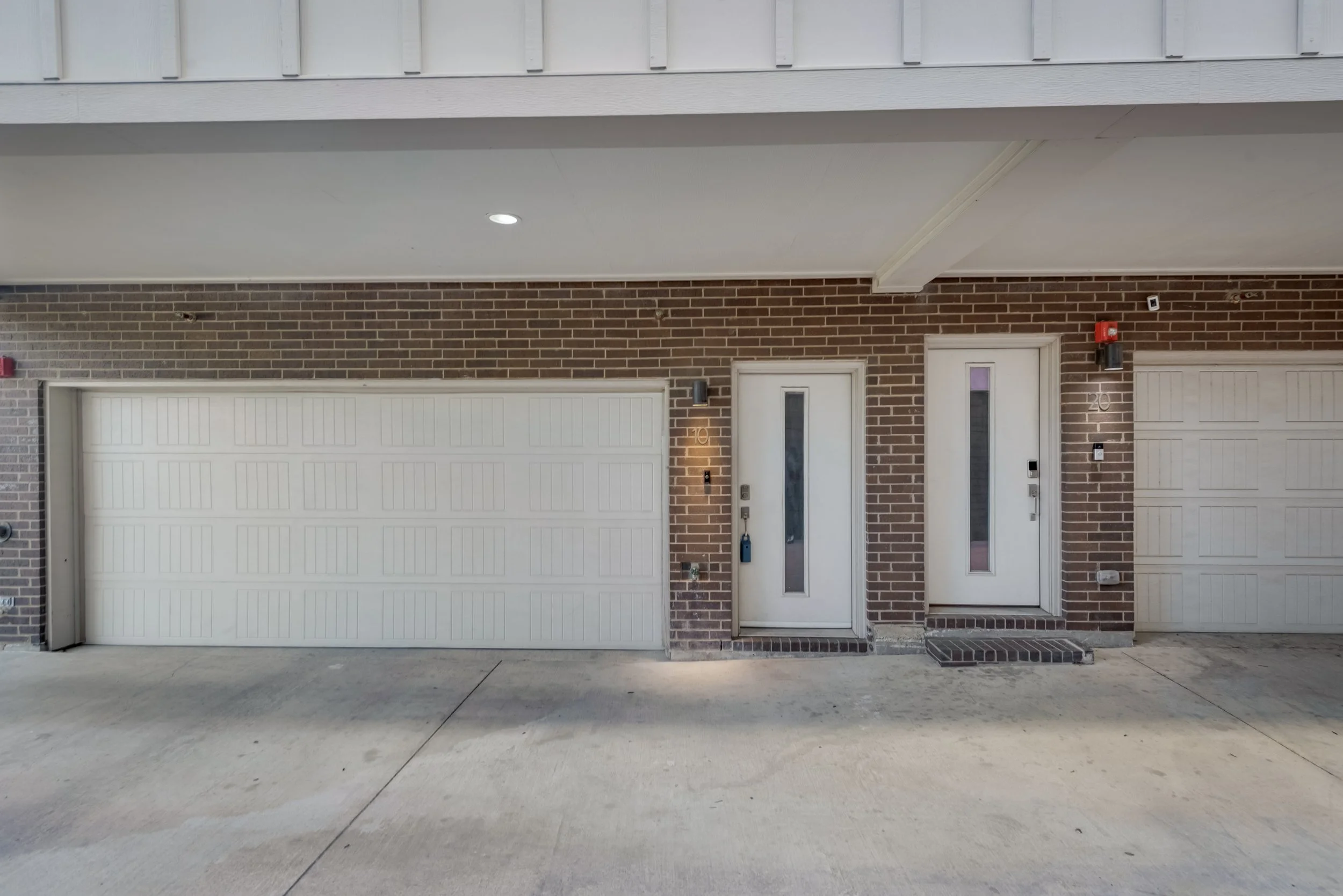 Front view of a residential building with a brick facade, a white garage door, two white entry doors, and a concrete driveway.