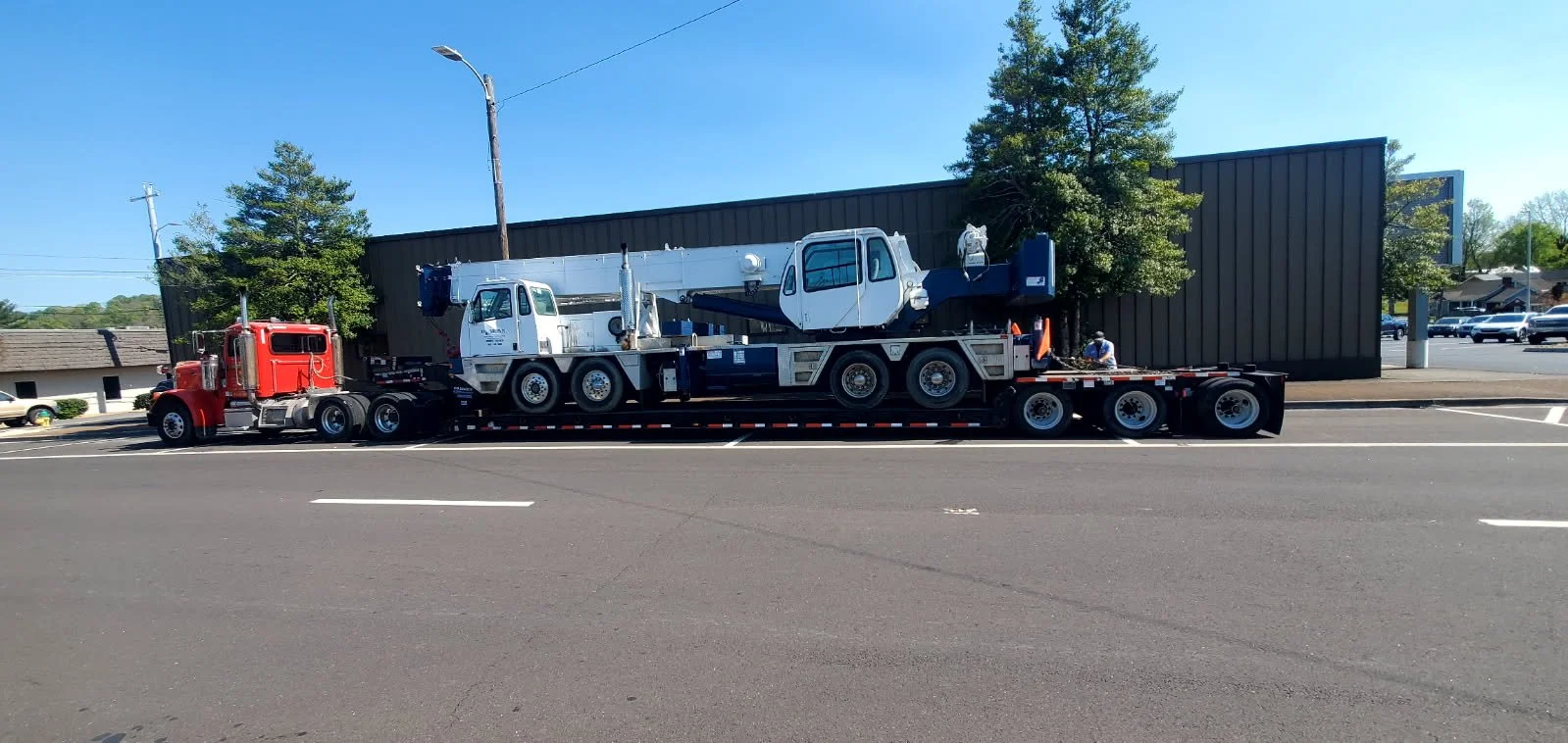 A large flatbed truck transporting a white construction crane on a city street during daytime.