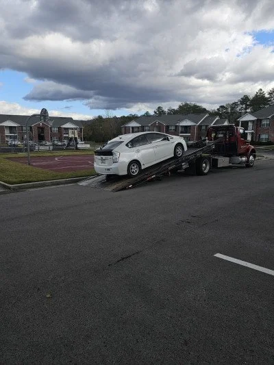 A white car being towed by a red tow truck on a residential street.