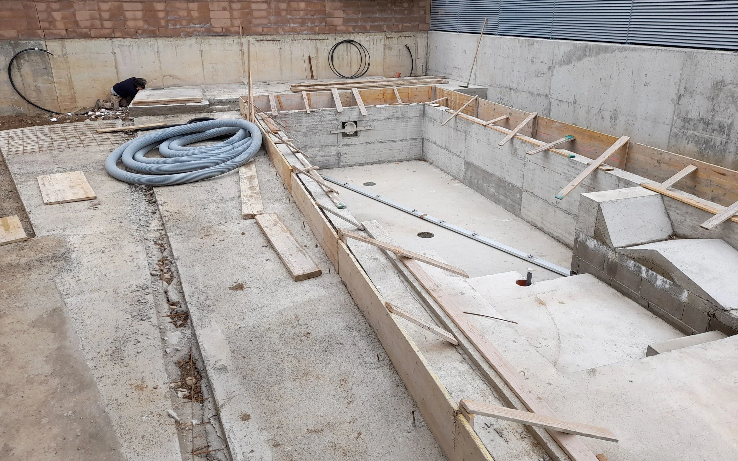 Baustelle mit Eingrabung für Pool, Holzrahmen und Bauwerkzeuge, Arbeiter bei der Arbeit.
