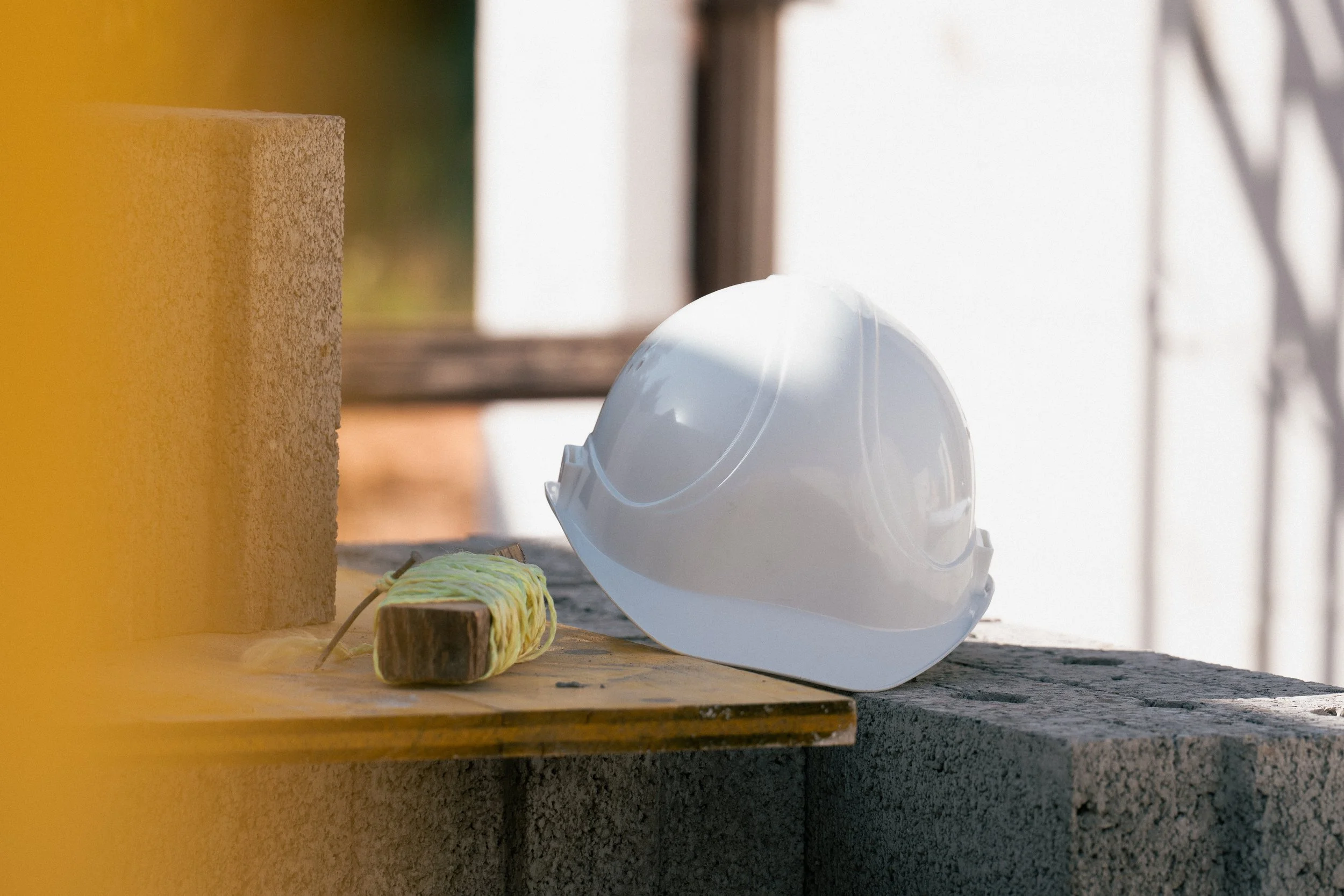 Bauhelm liegt auf einer Holzplatte neben einem Farbrad, auf einer Baustelle mit Geländer im Hintergrund.