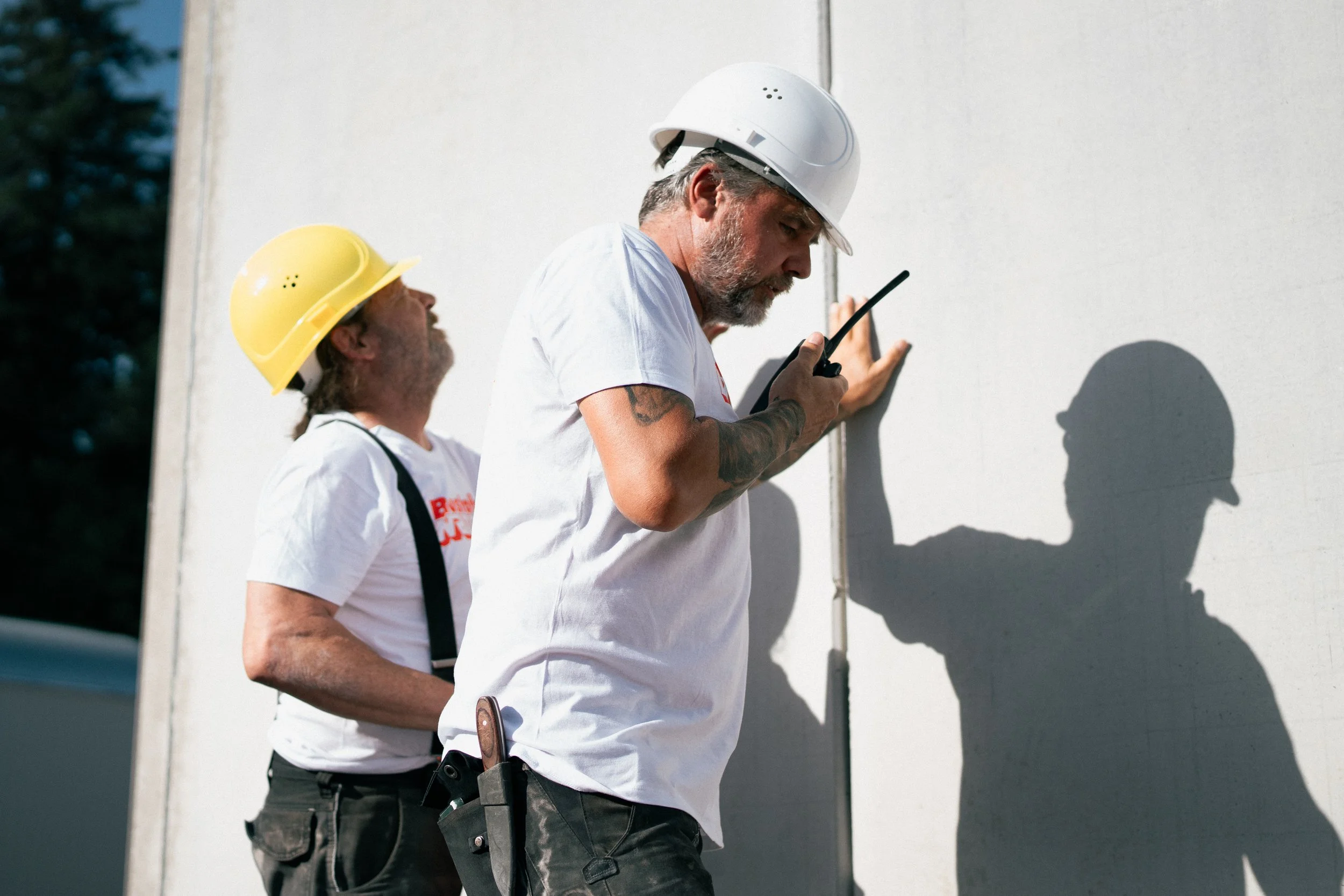 Zwei Bauarbeiter mit Helmen, die an einer weißen Wand stehen. Sie diskutieren oder planen etwas.