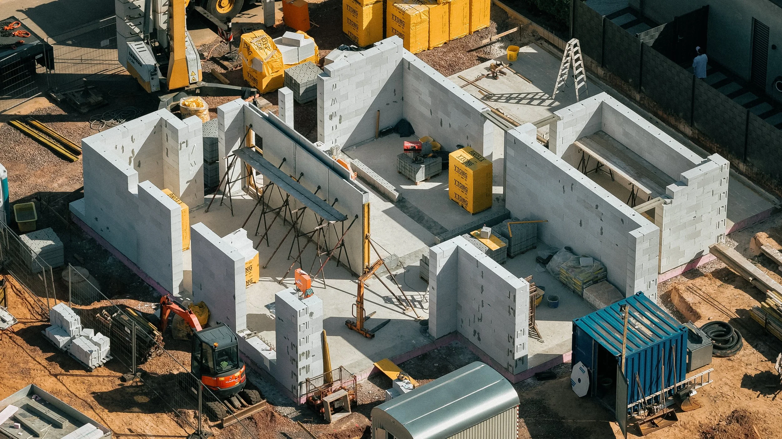 Bau eines Hauses mit weißen Ziegelwänden, Bauausrüstung und Baumaterialien auf einer Baustelle.