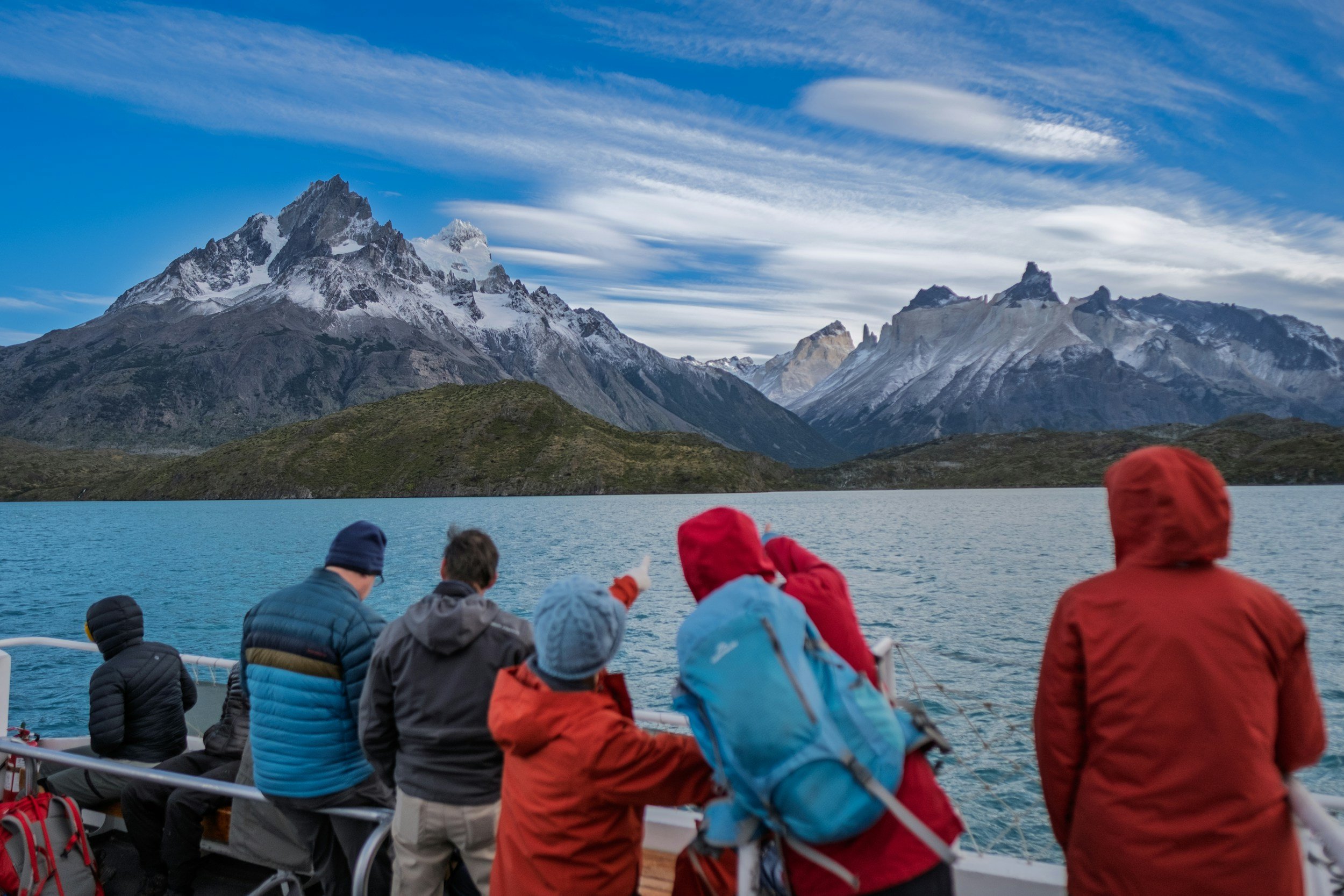 Multigenerational trip on a boat tour looking at snow-capped mountains with a partly cloudy sky.