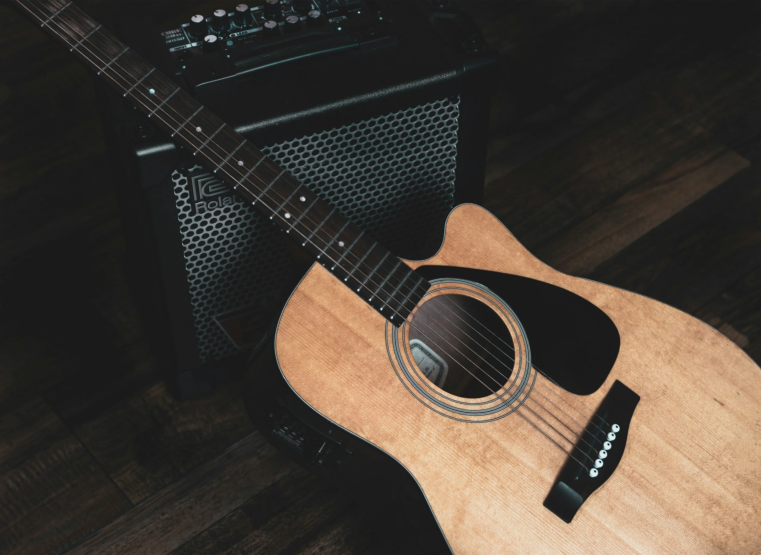 Acoustic guitar resting on an amplifier, with an effects pedal on top of the amplifier and a dark wooden floor.