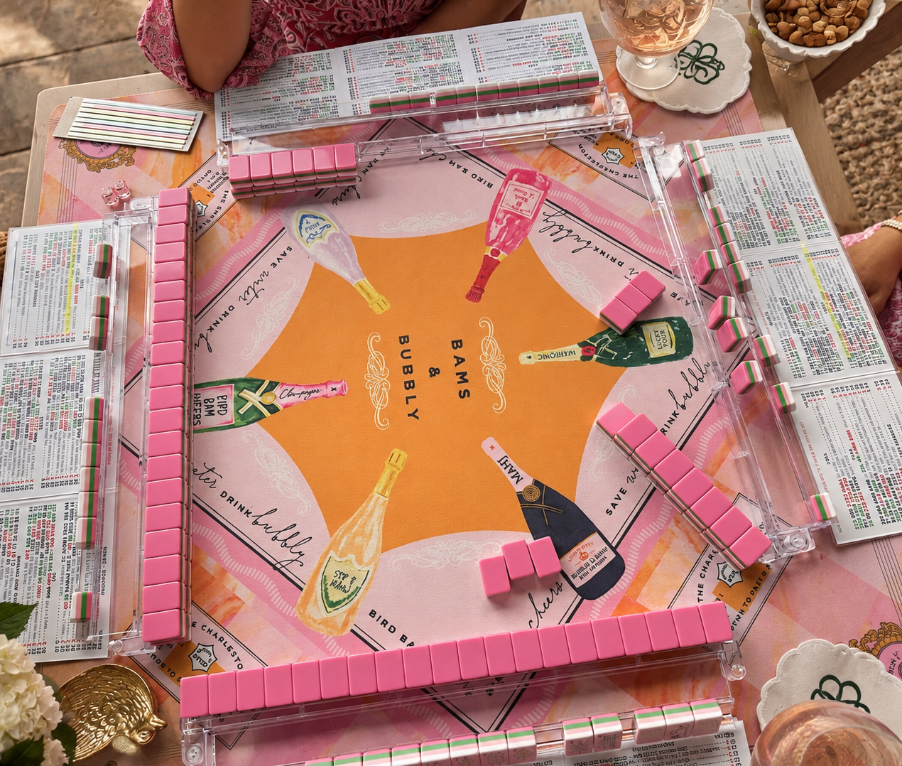 A table set up for playing Bams & Bubbly, a lemon and strawberry-themed game, with pink tiles, champagne bottles, and beverage menus.