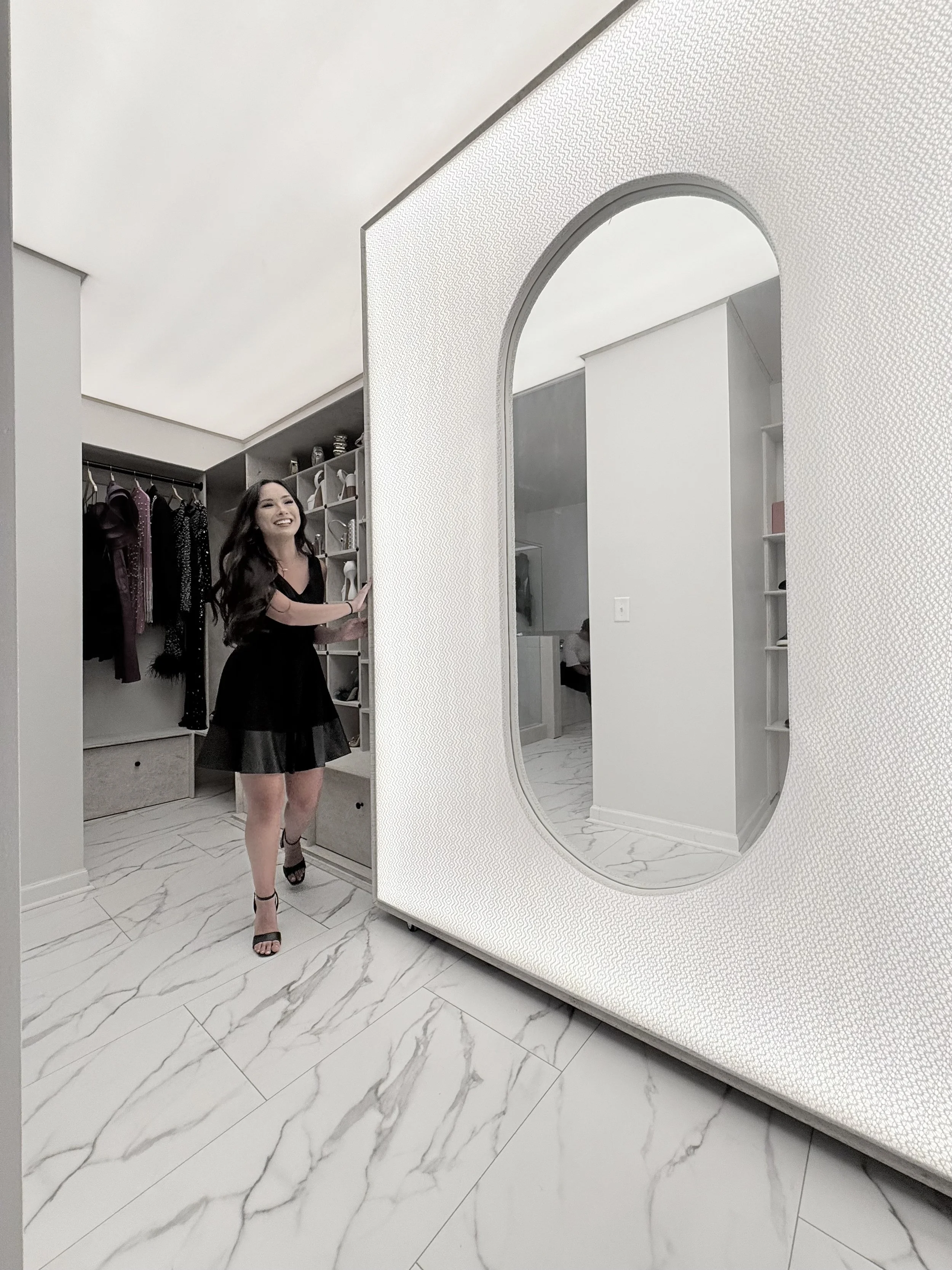 A modern, stylish closet with a large oval luxury futuristic mirror with lighting, and lit ceiling.