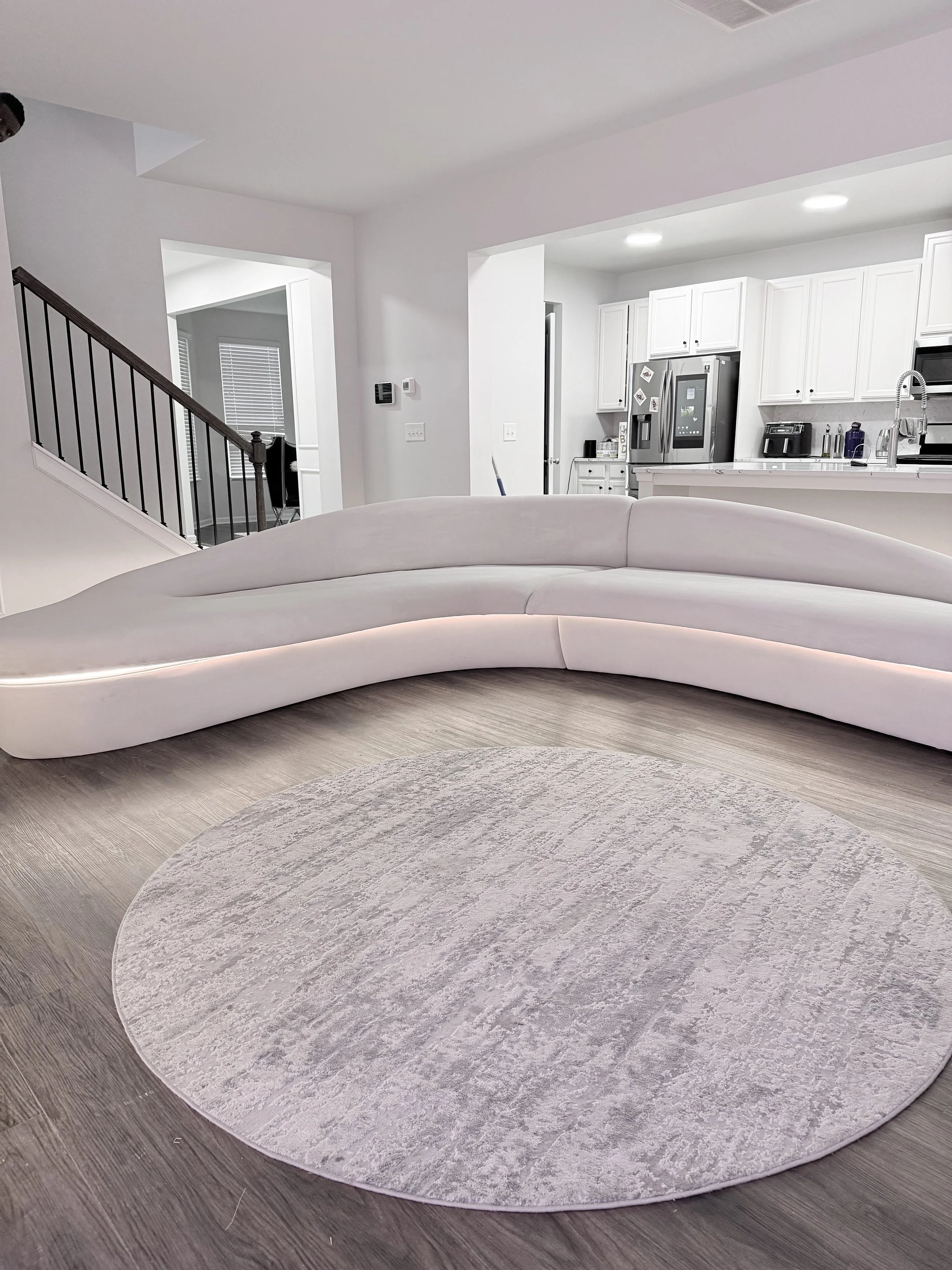 A modern living room with a white curved sofa, a round light-colored rug. Beluga sofa