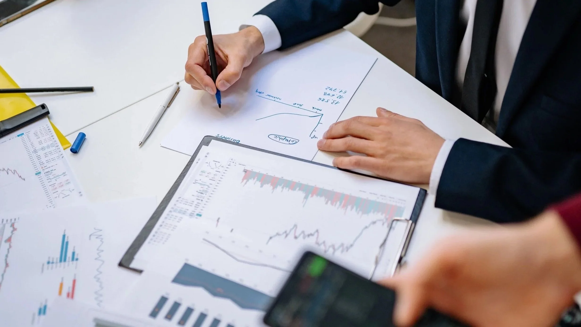 Personne en costume analysant des graphiques financiers et des notes lors d'une réunion d'affaires.