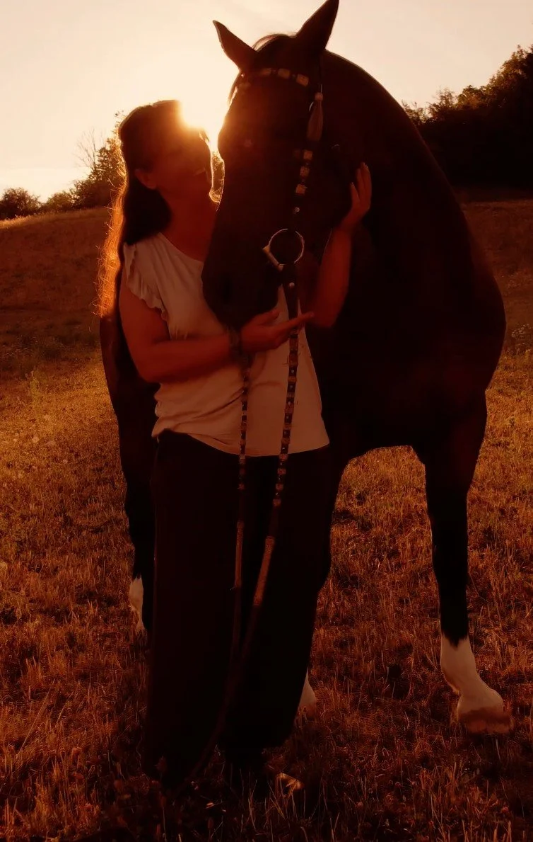 Frau hält ein Pferd bei Sonnenuntergang im Freien.