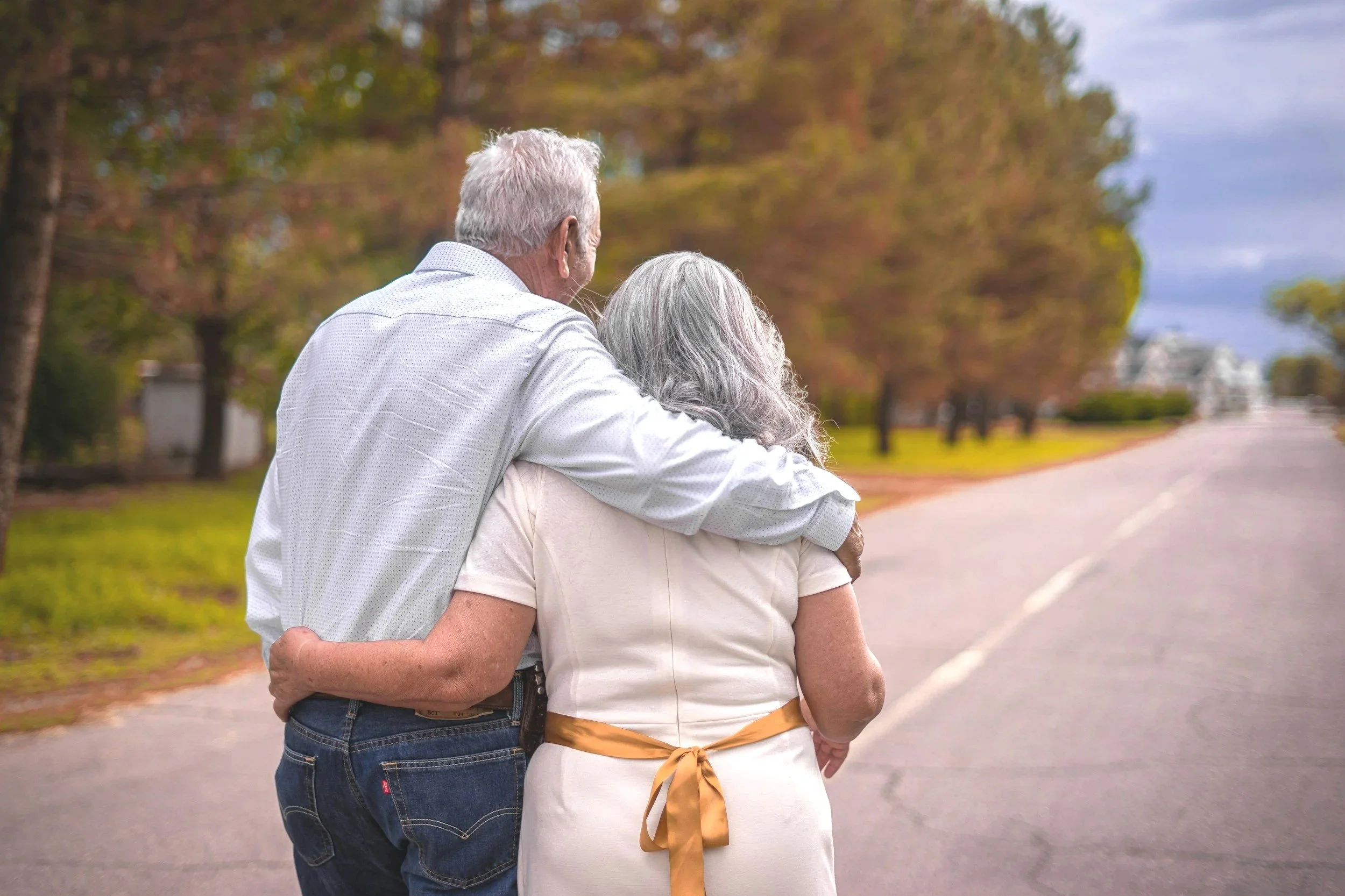 Older couple walking outdoors in autumn, with the man resting his arm on the woman's shoulder.