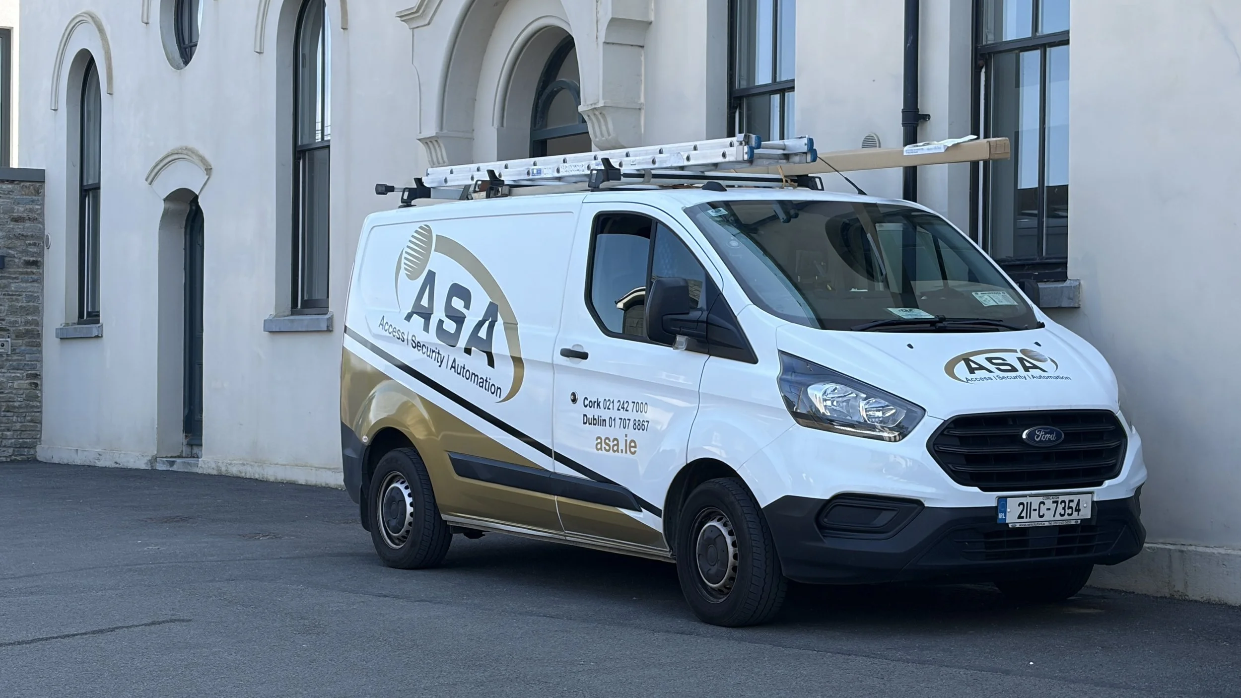 White van with the logos and contact information of ASA Access Security Automation parked in front of a building with arched windows and a white facade.
