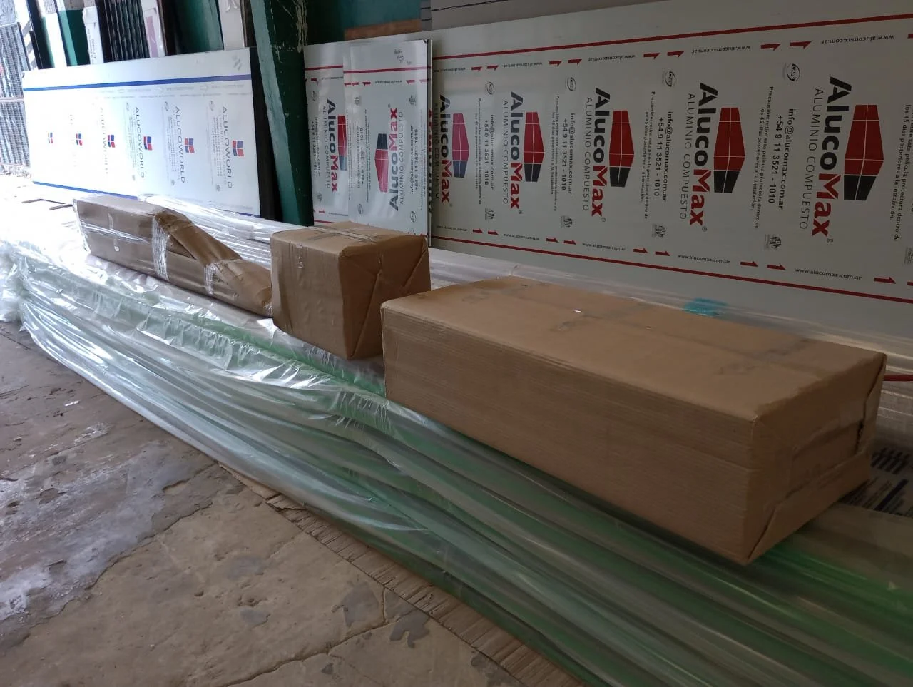Construction materials including insulated panels, wrapped pipes, and wooden blocks stored on a construction site floor.