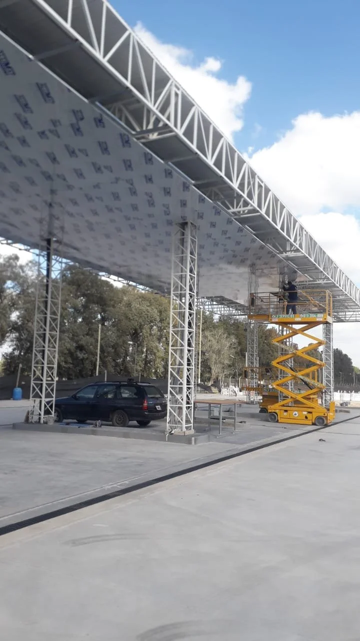 Construction worker on yellow scissor lift installing or repairing a large elevated metallic structure outdoors on a sunny day.