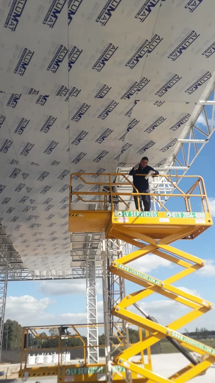 Worker on yellow hydraulic lift installing or repairing a roof with insulation tiles labeled ALUMAT.