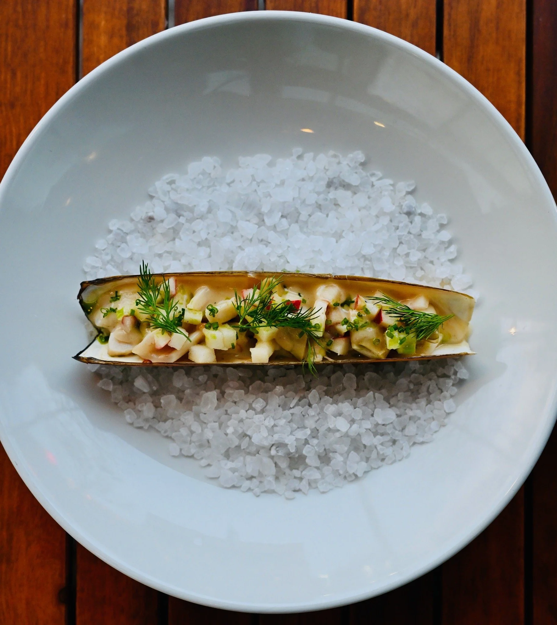 A white bowl filled with coarse sea salt, placed on a wooden surface.