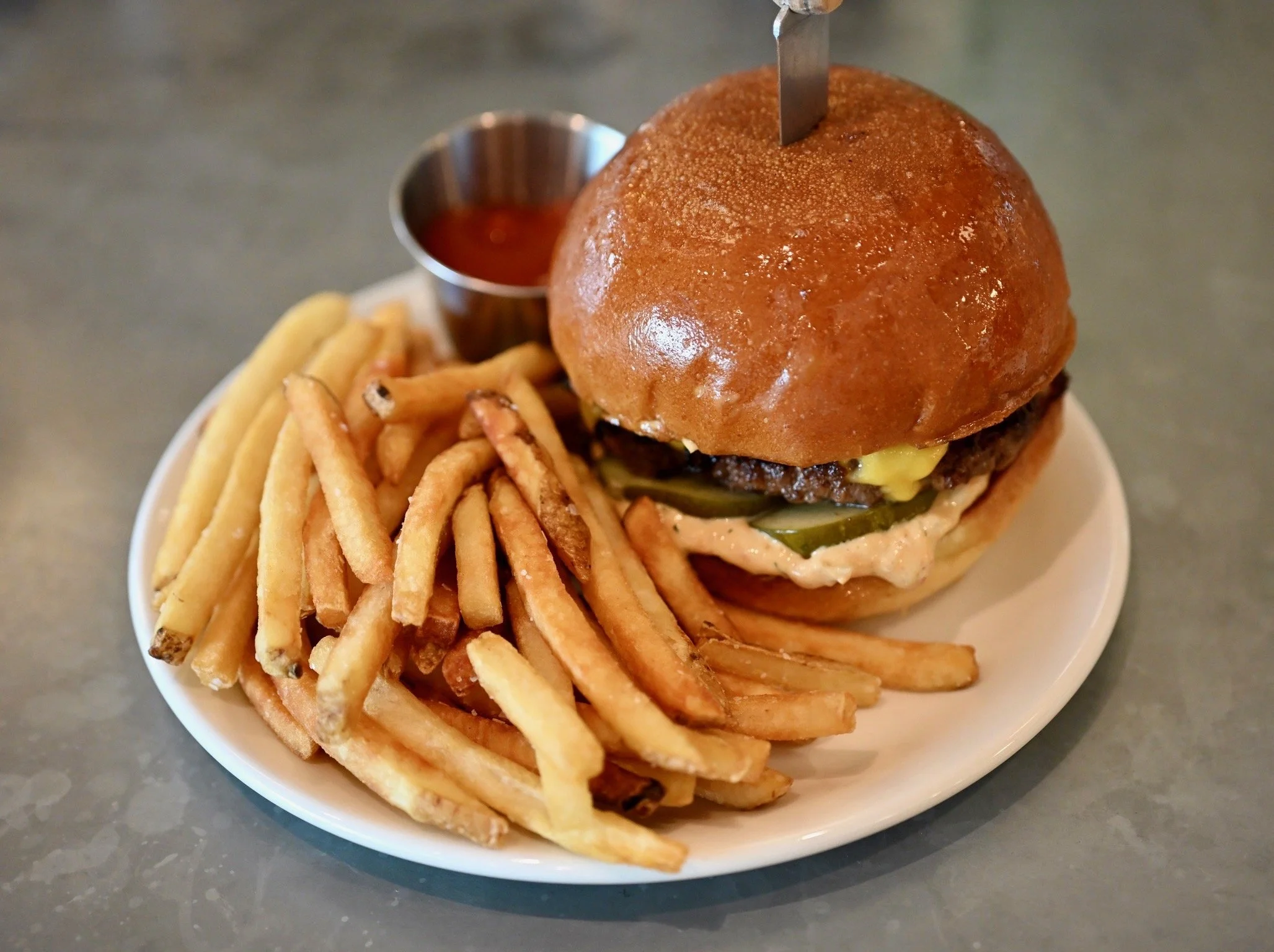 A plate with French fries and a cheeseburger with toppings including pickles and melted cheese, served with a side of ketchup.