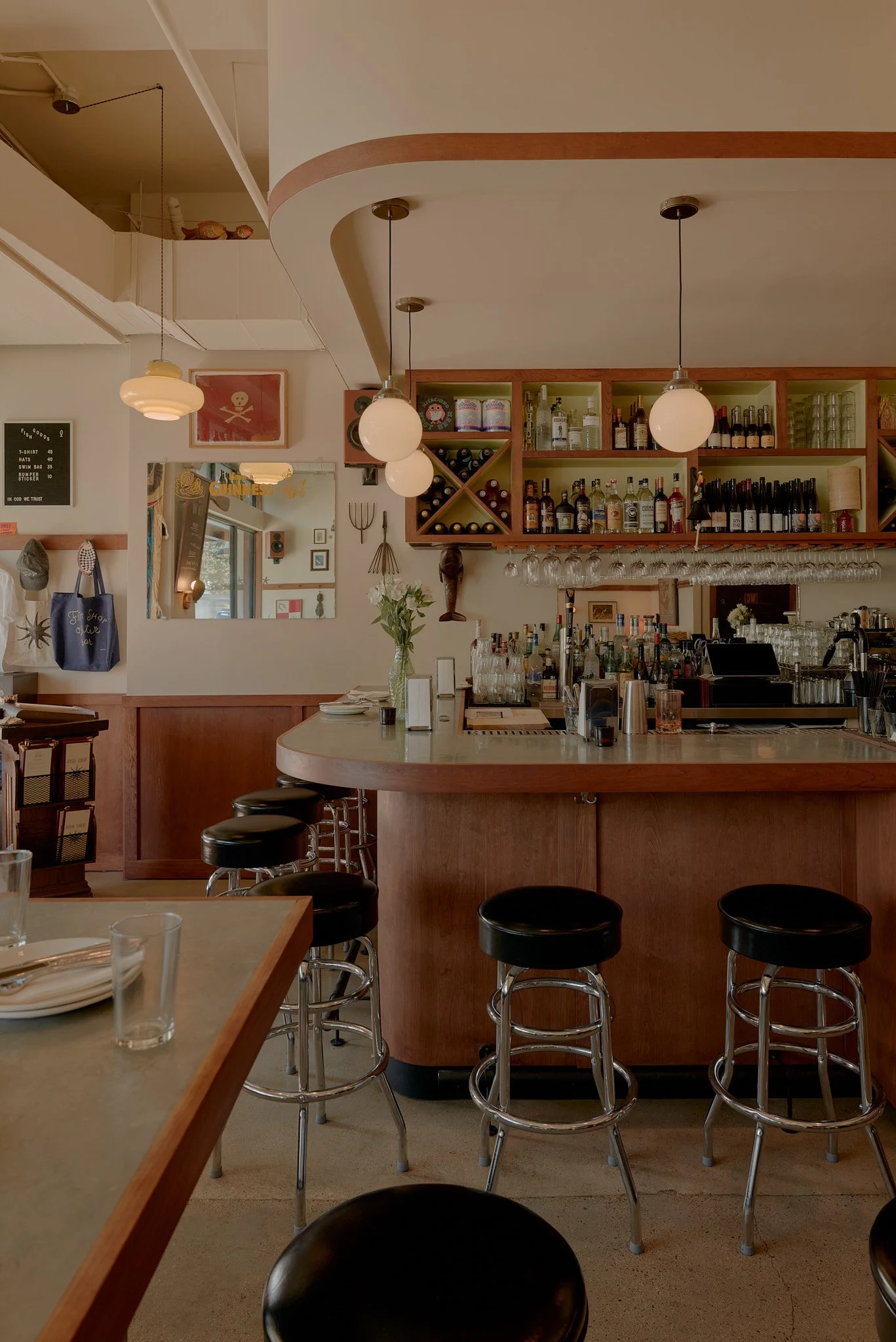 Interior of a bar or restaurant with a curved bar counter, barstools, shelves with bottles of alcohol, hanging wine glasses, and various decorations.
