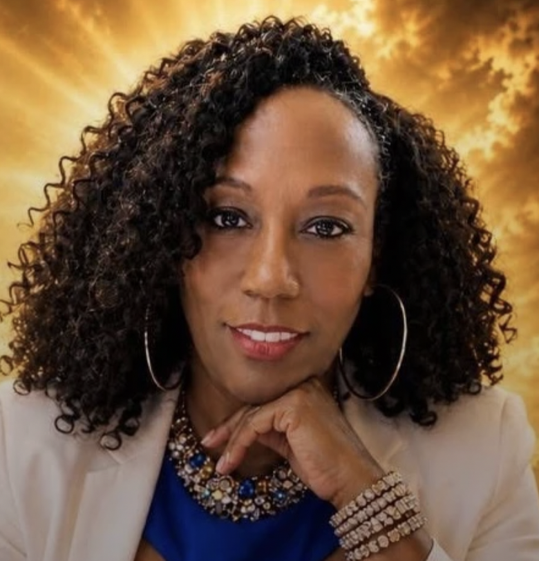 A woman with curly dark hair, wearing a beige blazer, blue top, large hoop earrings, and multiple pearl necklaces, against a golden cloudy sky background.