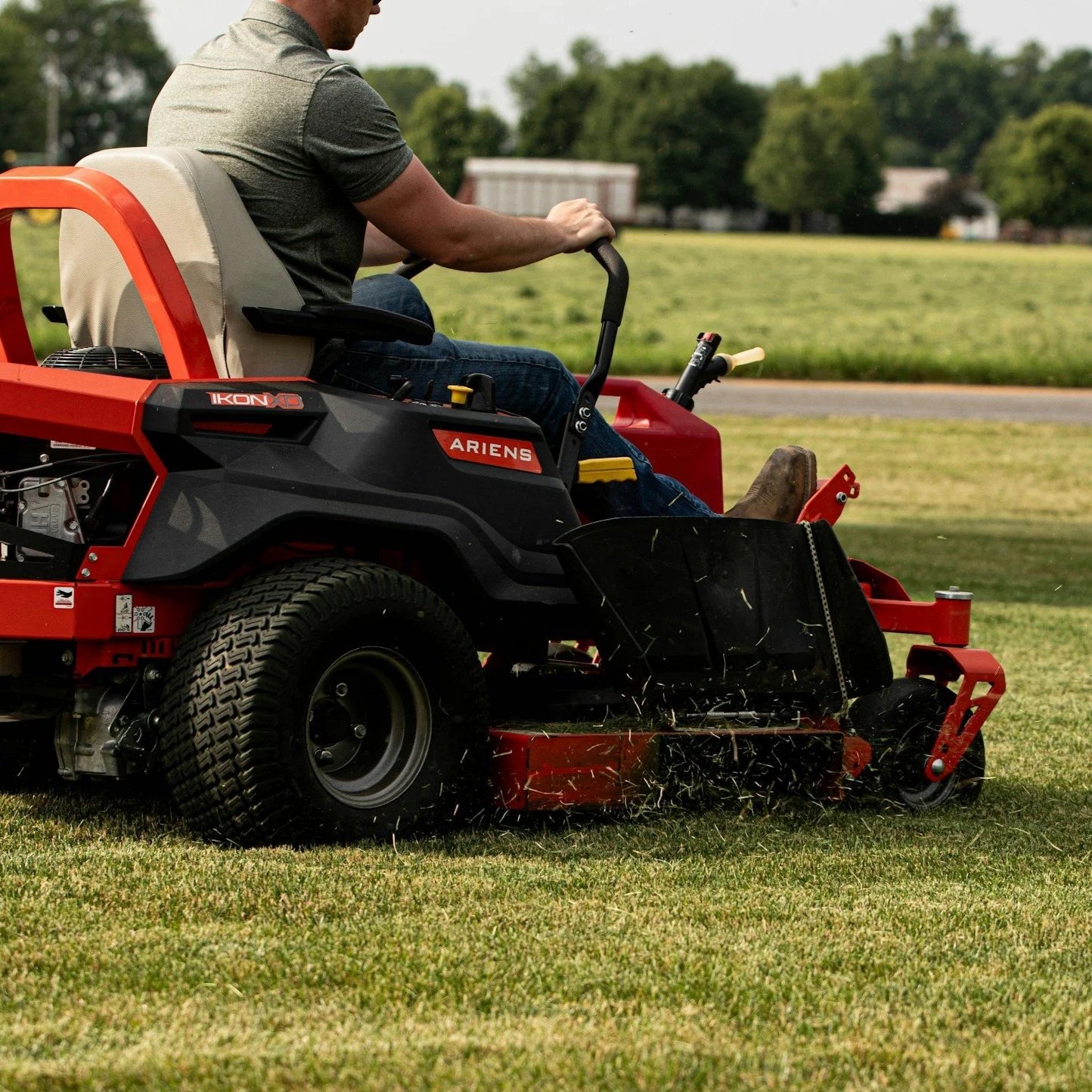 A person operating a red and black Ariens riding lawn mower on a grassy field, cutting the grass.