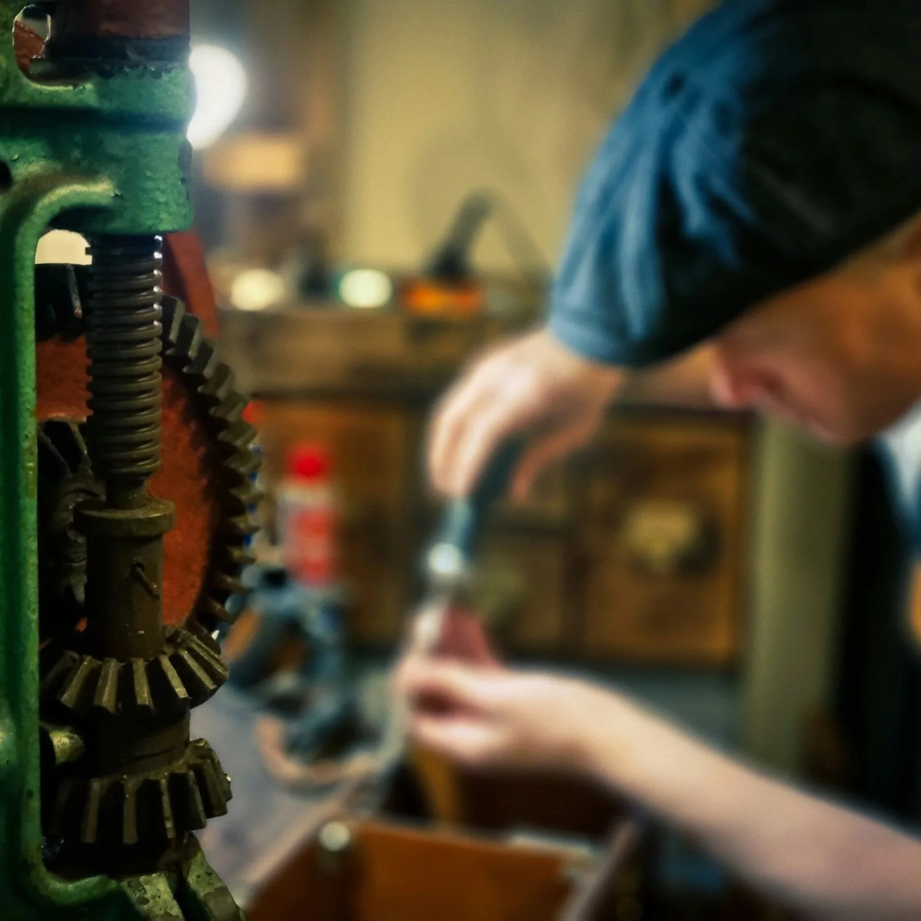 Close-up of a gear mechanism with a person in the background working on a project in a workshop.
