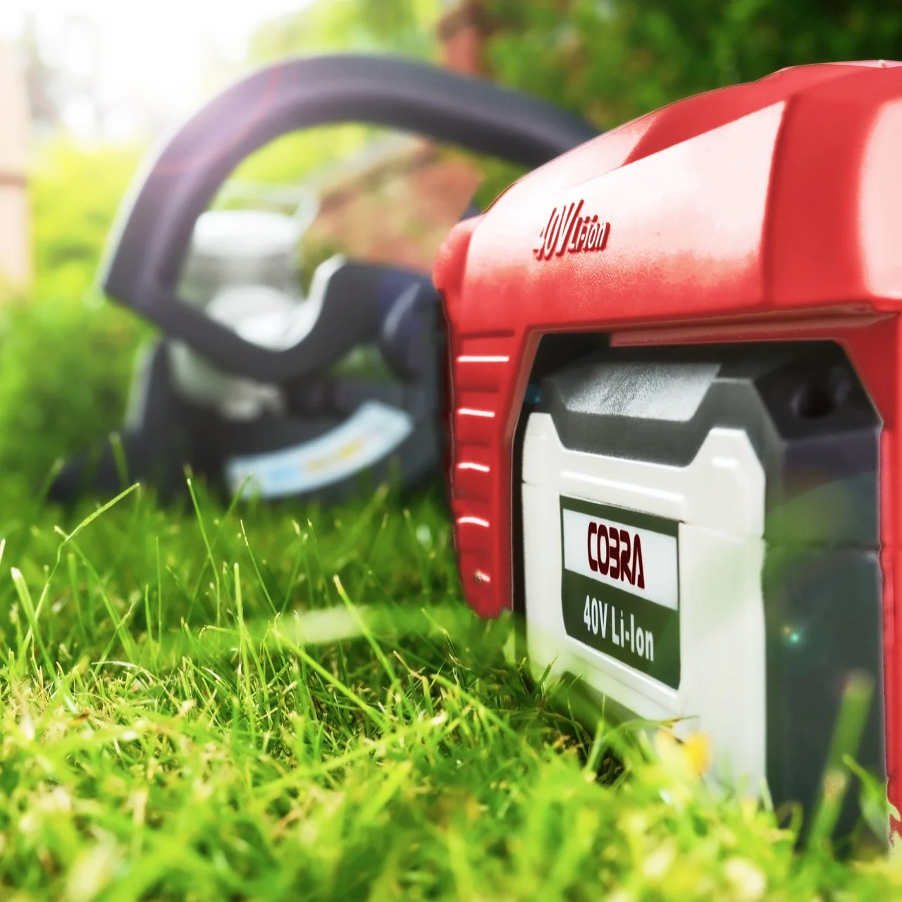 Close-up of a red and white Cobra 40V Li-ion chainsaw battery placed on green grass with blurred background.
