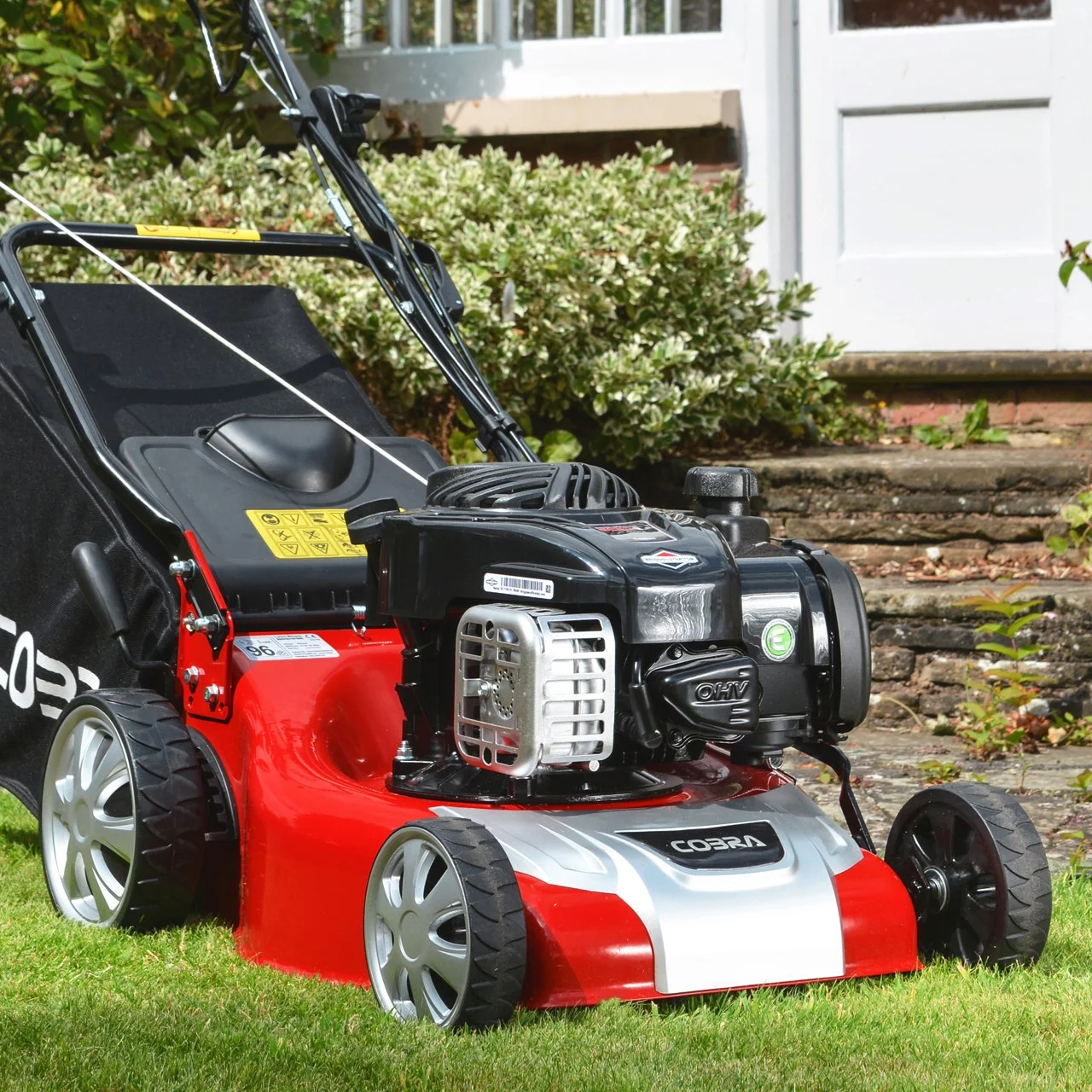 A red and black gas-powered lawn mower sitting on green grass outside a house.