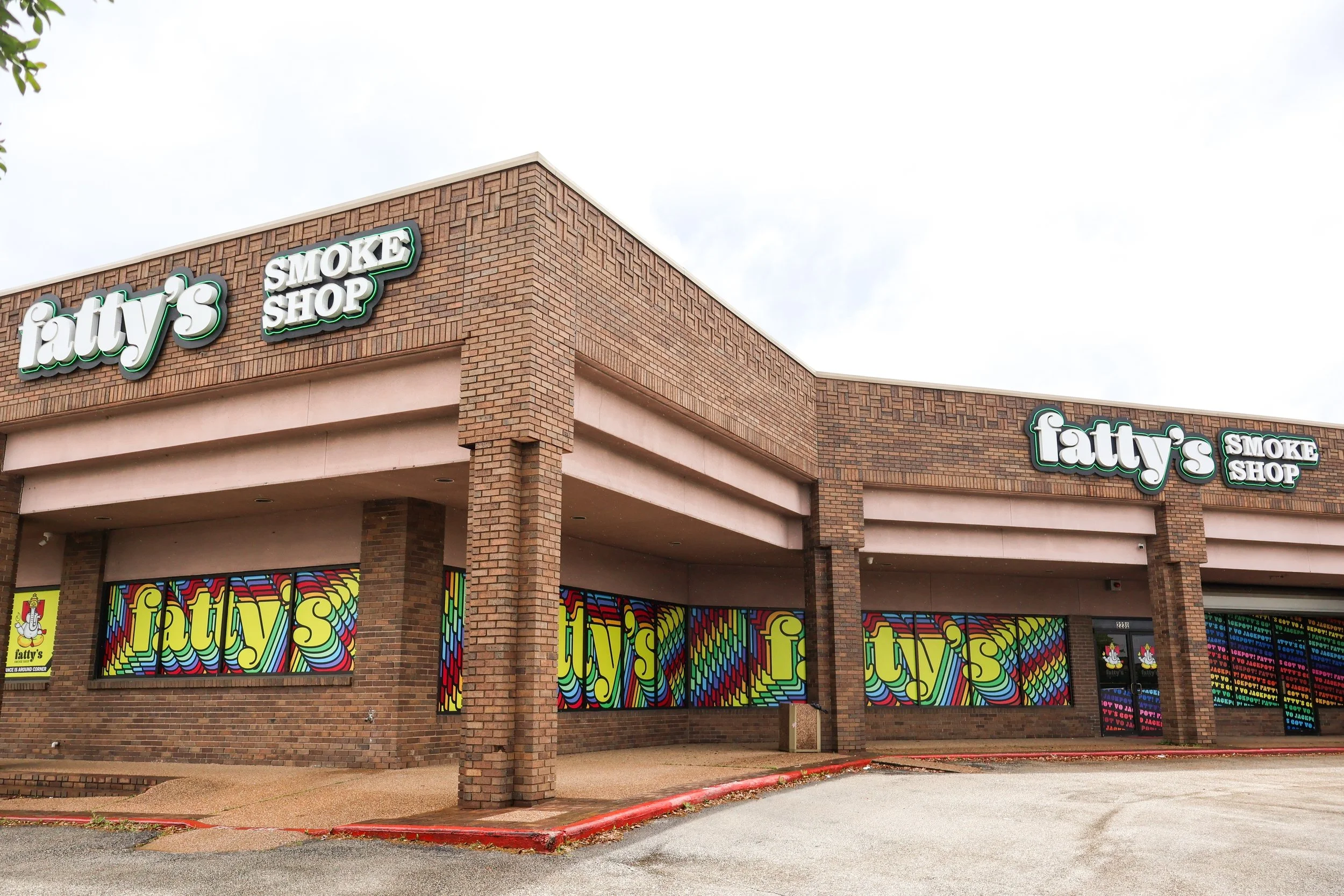 Exterior view of a College Station brick building with signs that say "fatty's" and "smoke shop" on the upper part. The storefront features colorful, psychedelic-style window coverings with the "fatty's" logo repeated.