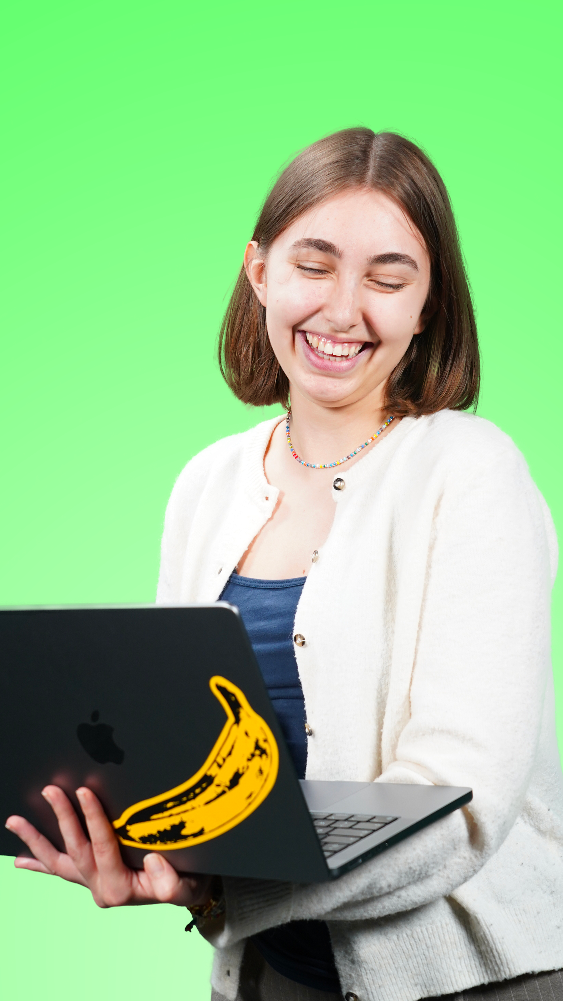 Jeune femme souriante, tenant un ordinateur portable avec un autocollant de banane, se tenant devant un fond vert.