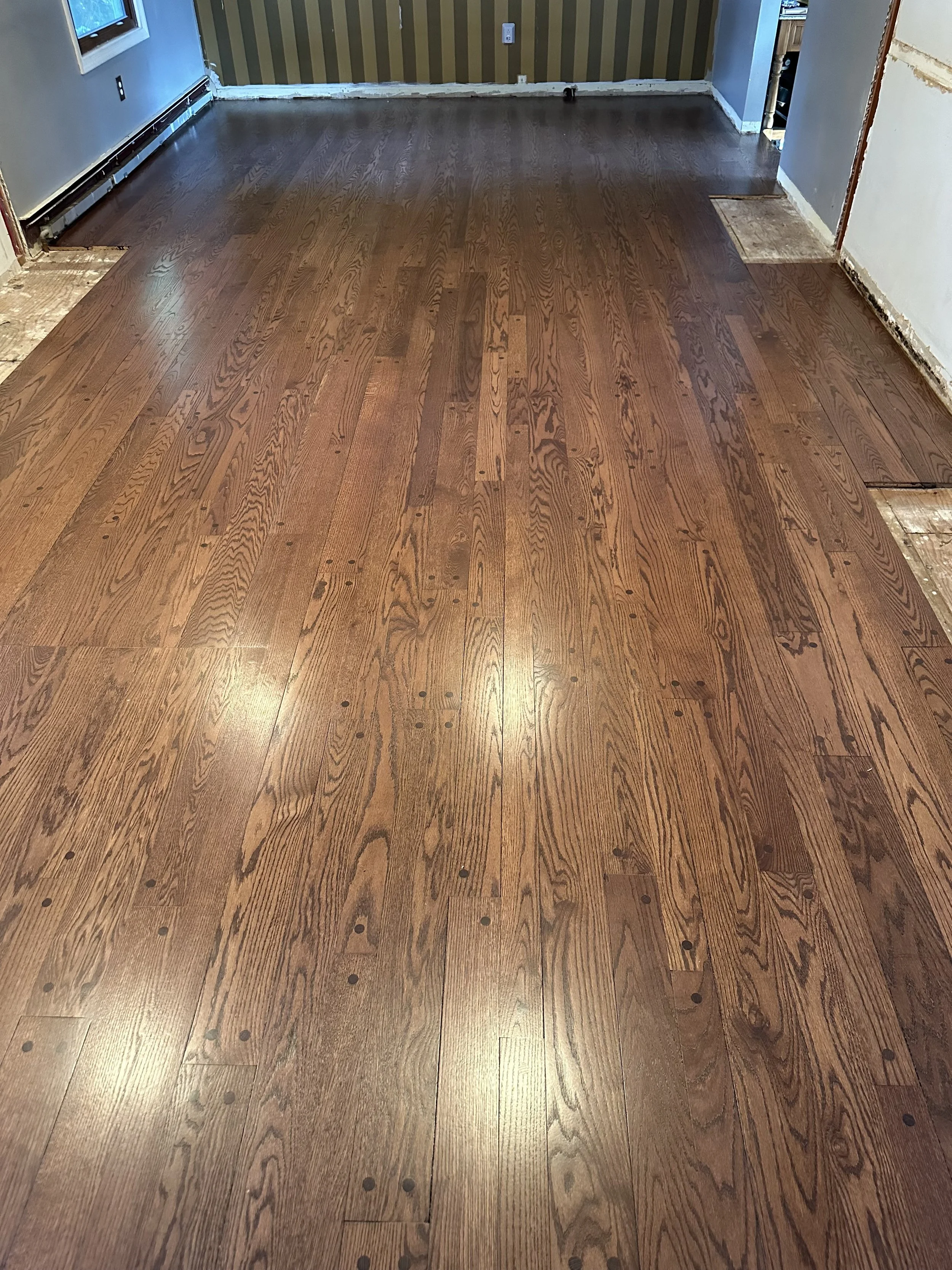 Room with hardwood floors, partially installed, with some floorboards missing and visible nails, and a partially finished wall.