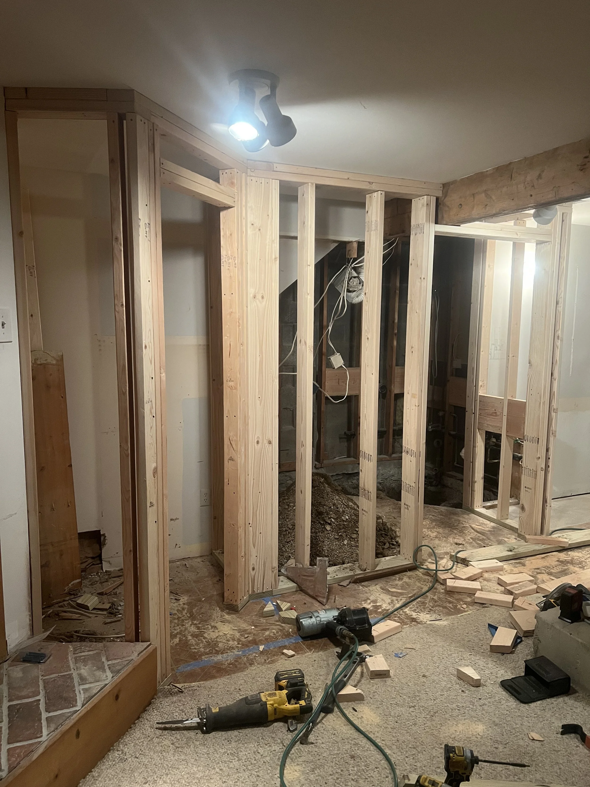 Interior view of a room under renovation with wooden framing, construction tools, and scattered construction materials.