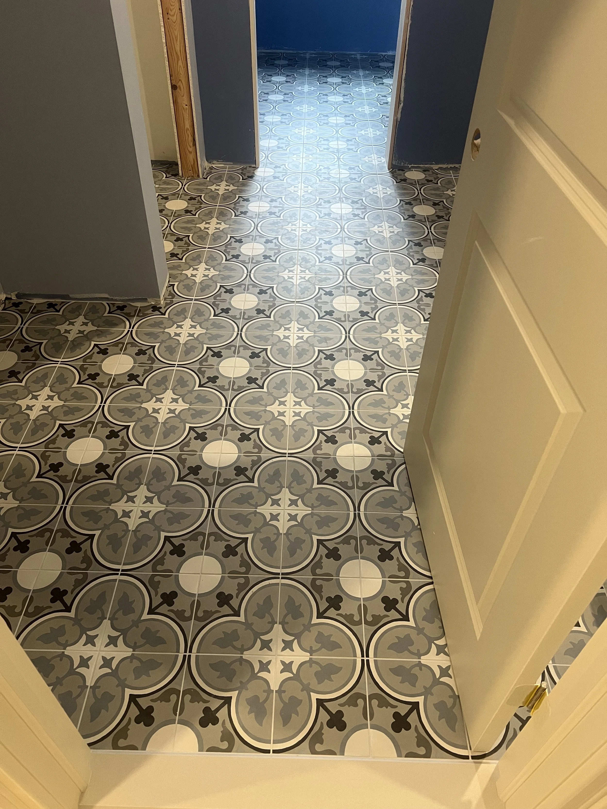 View of a doorway with black and white patterned tile floor, white entrance trim, and a door left open showing an interior with blue walls and matching patterned tile flooring.