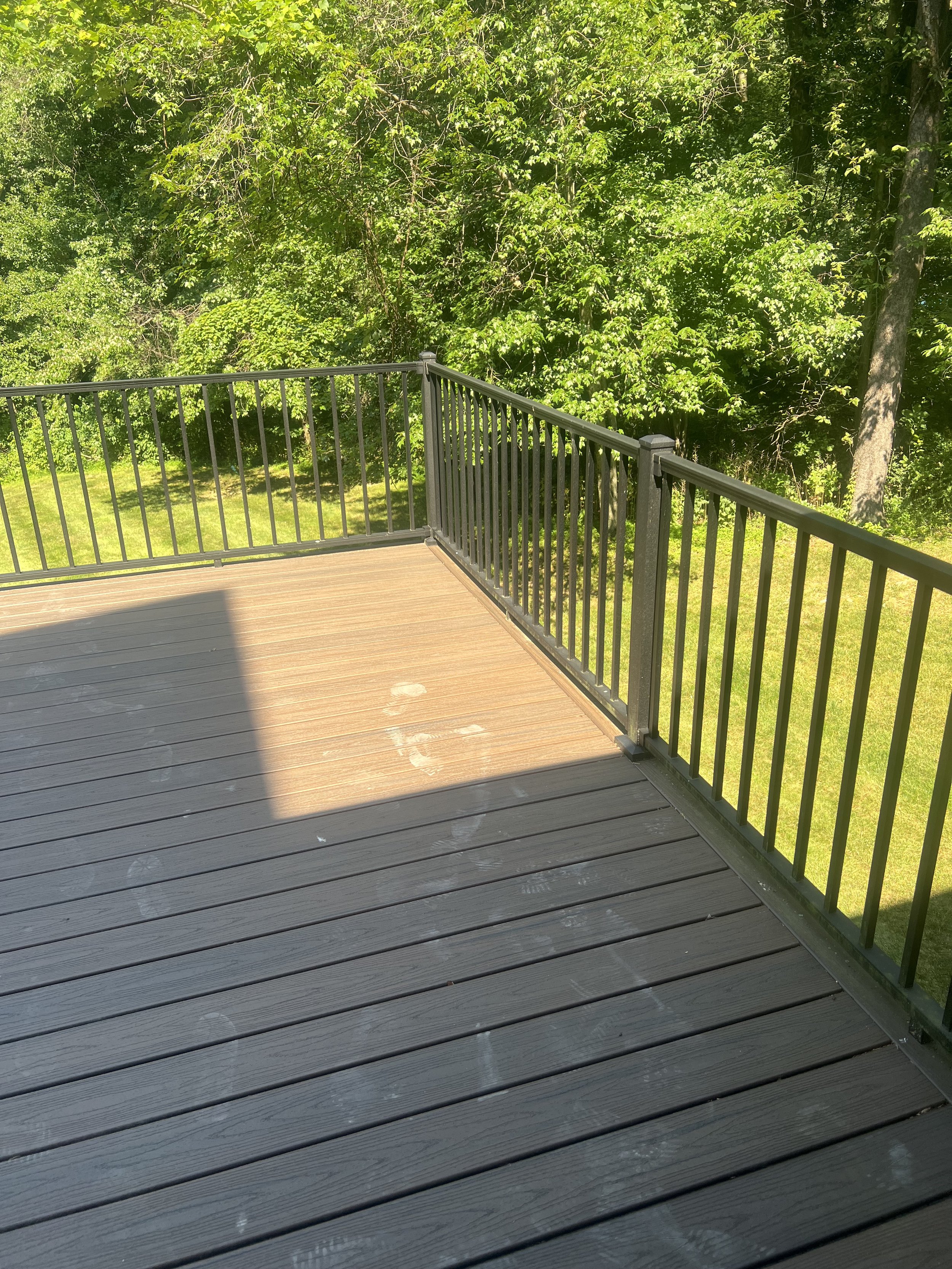 A wooden deck with a black metal railing, overlooking a lush green wooded area.